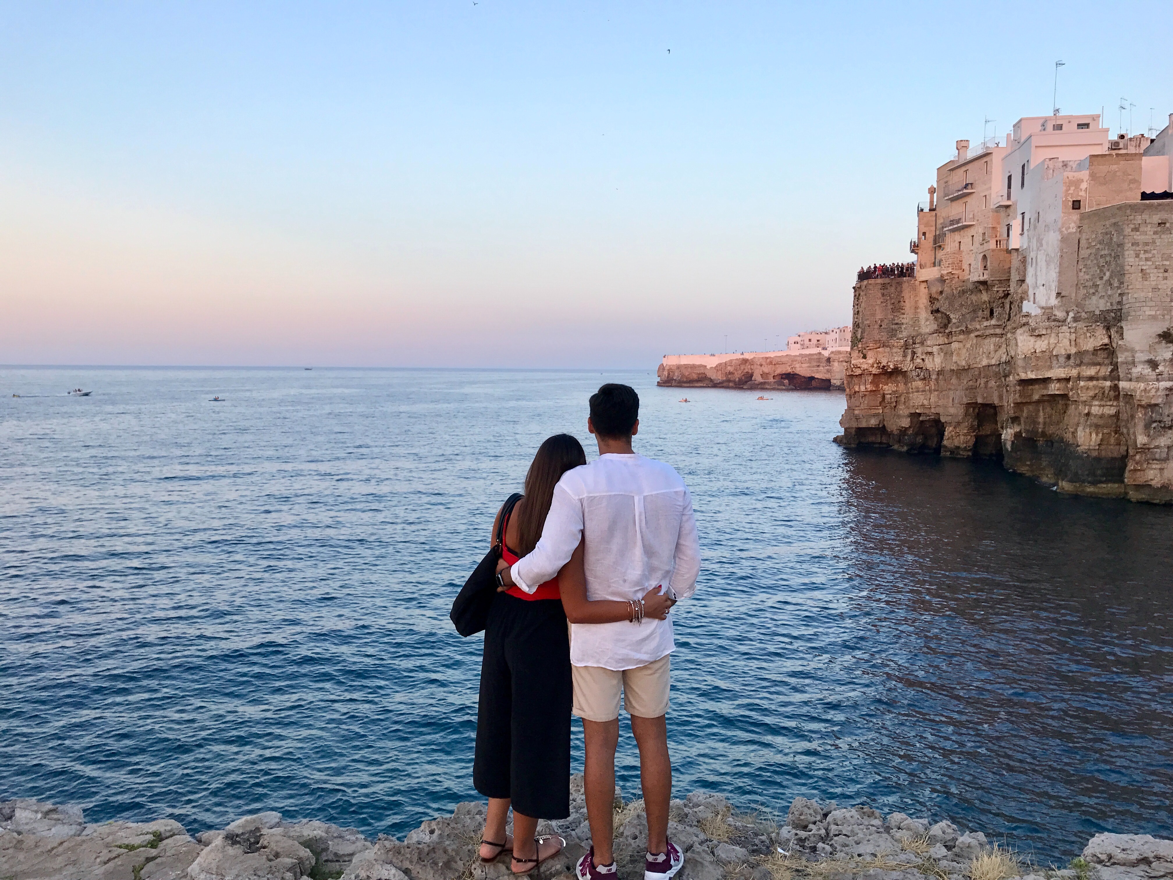 Man in white dress shirt standing beside the woman in black and red dress while watching the blue calm water near brown concrete buildings under white and blue sky at daytime photo