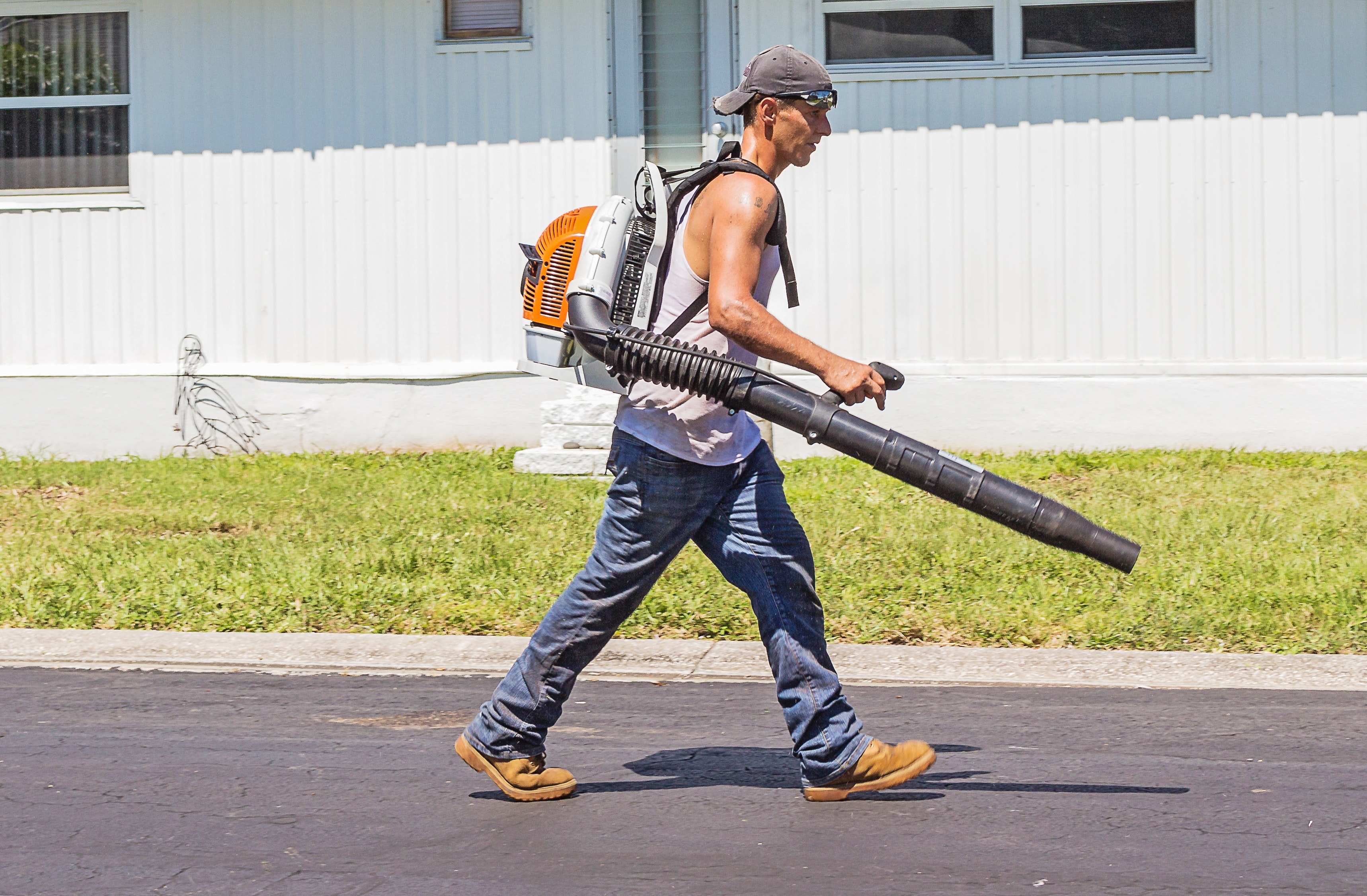 Man in white tank top and blue denim pants with leaf blower outdoors during daytime photo