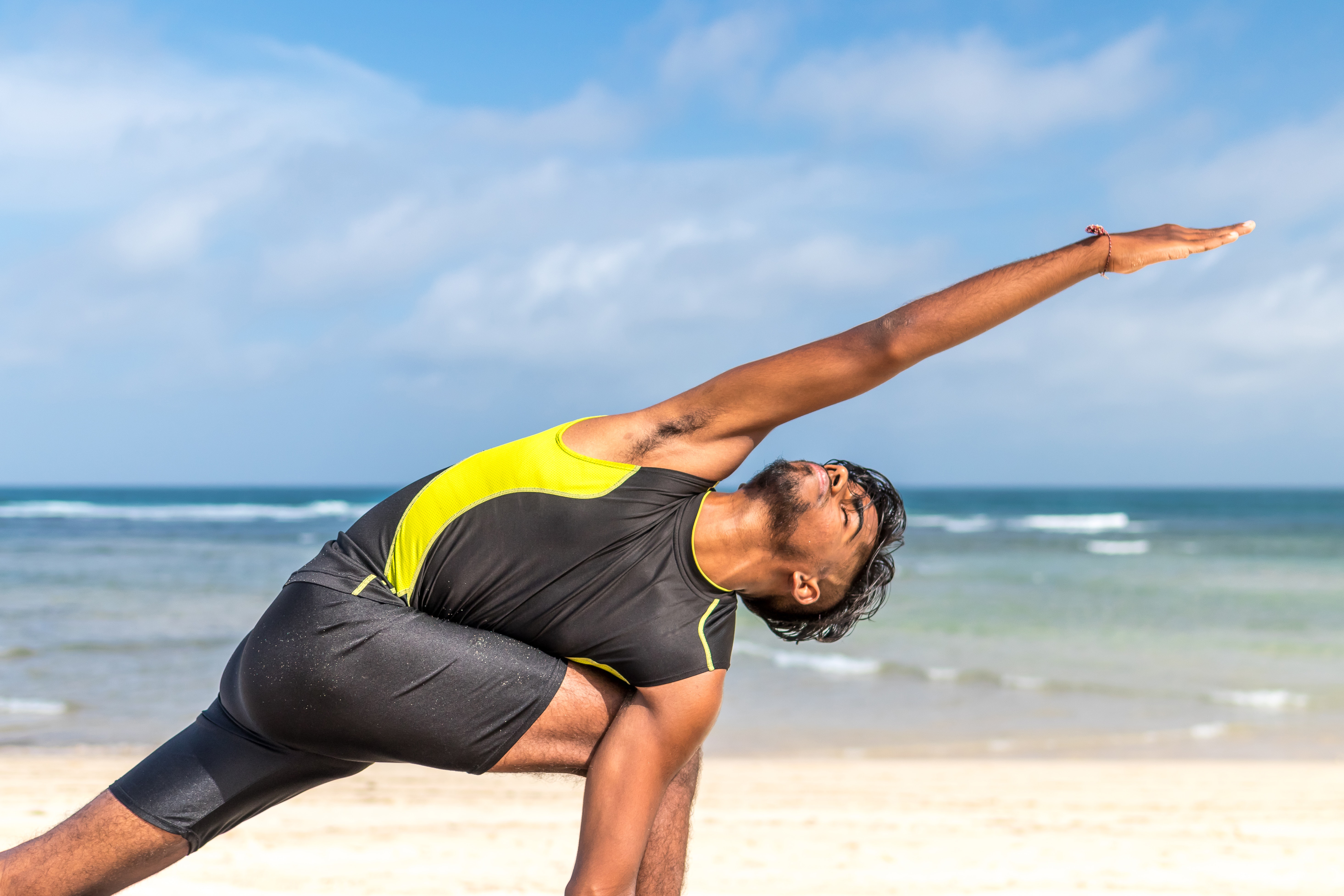 Man in yellow and black tank top doing exercise on seashore at daytime photo