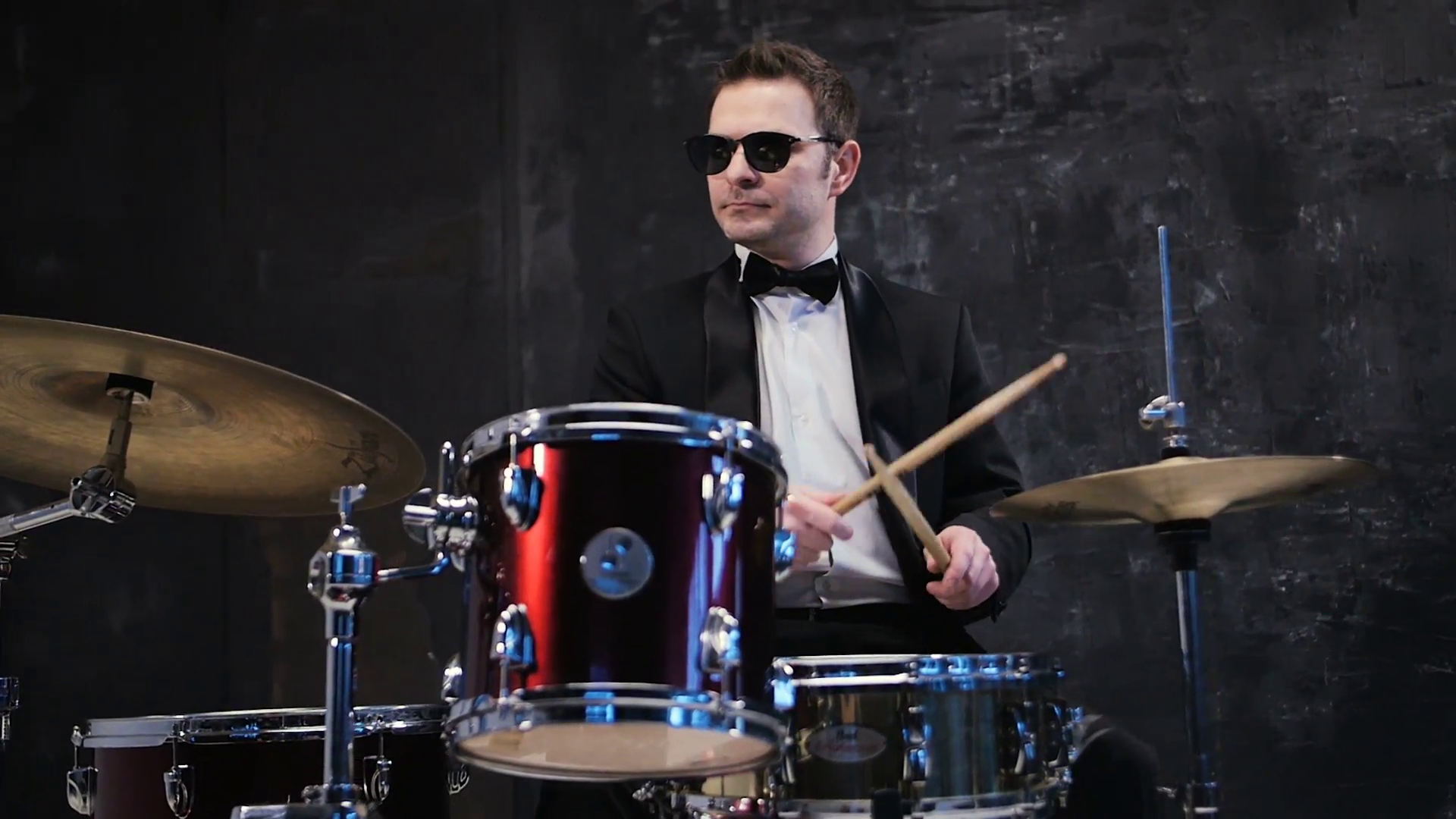Man in black suit and sunglasses plays on drum. Rock cover band ...