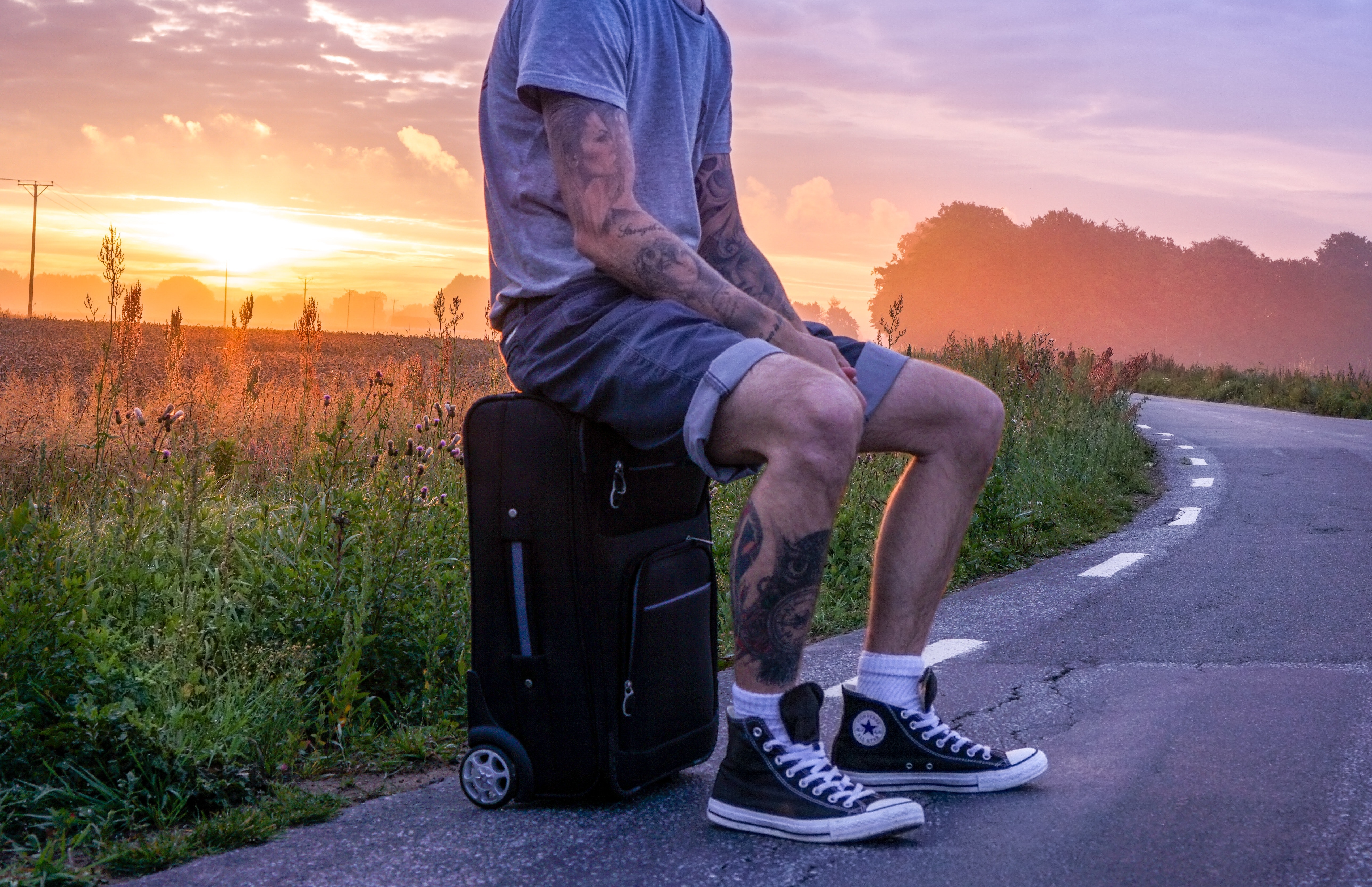 Man sitting on luggage on road side during sunset photo