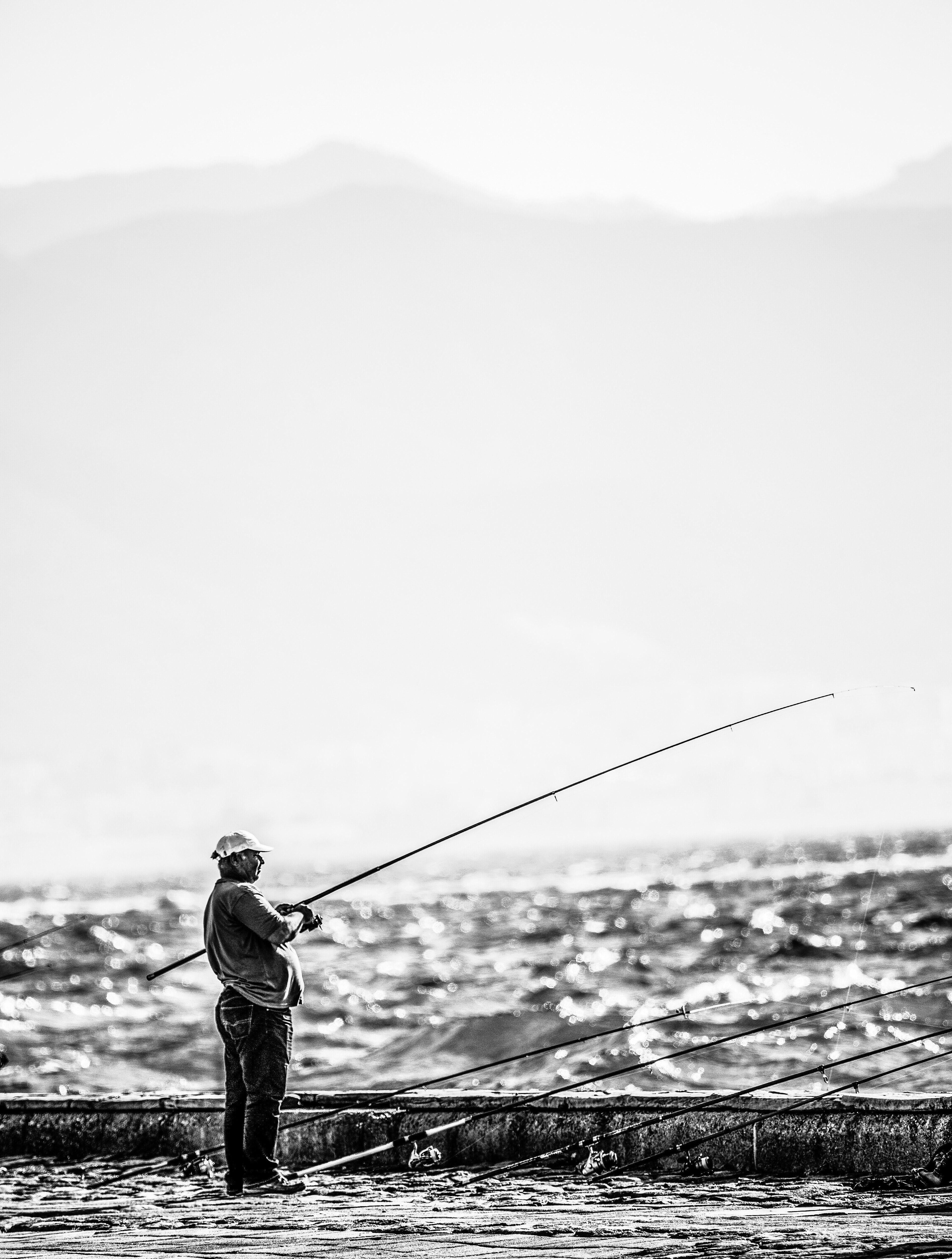 Man standing near seashore holding fishing rod on grayscale photography