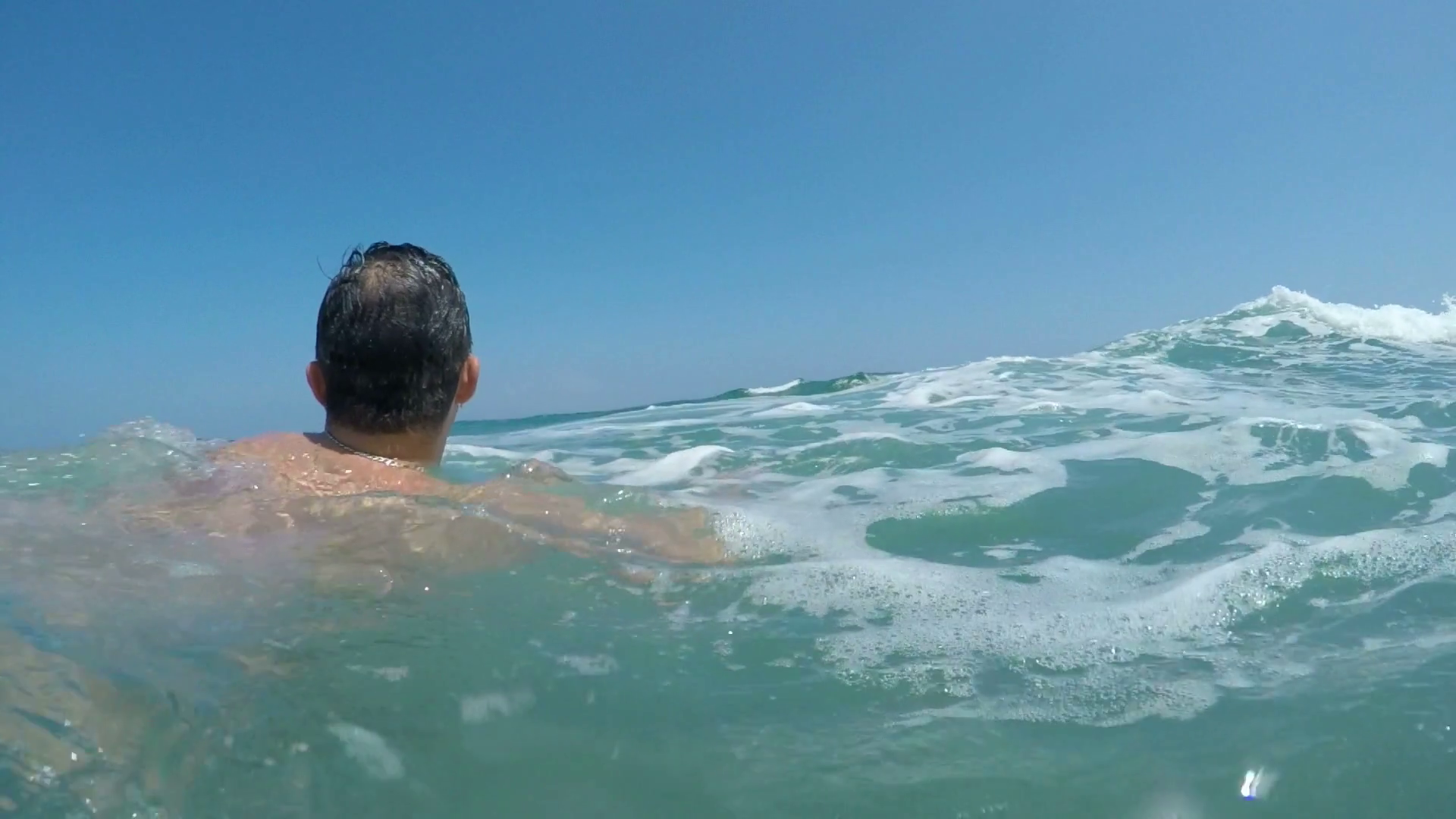 Back view of a man swimming in the waves of Alboran Sea in Andalusia ...
