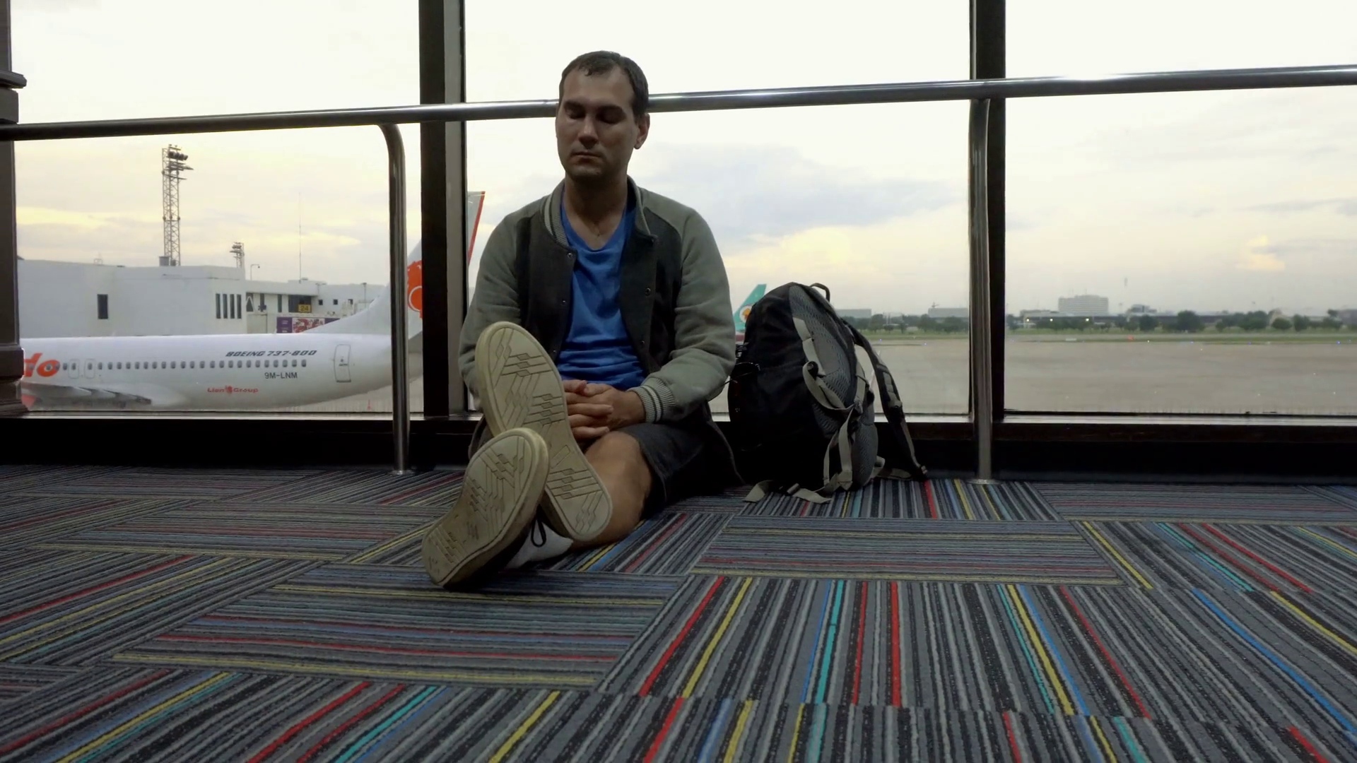 Man waiting for flight at airport sitting on the floor. Airplane ...