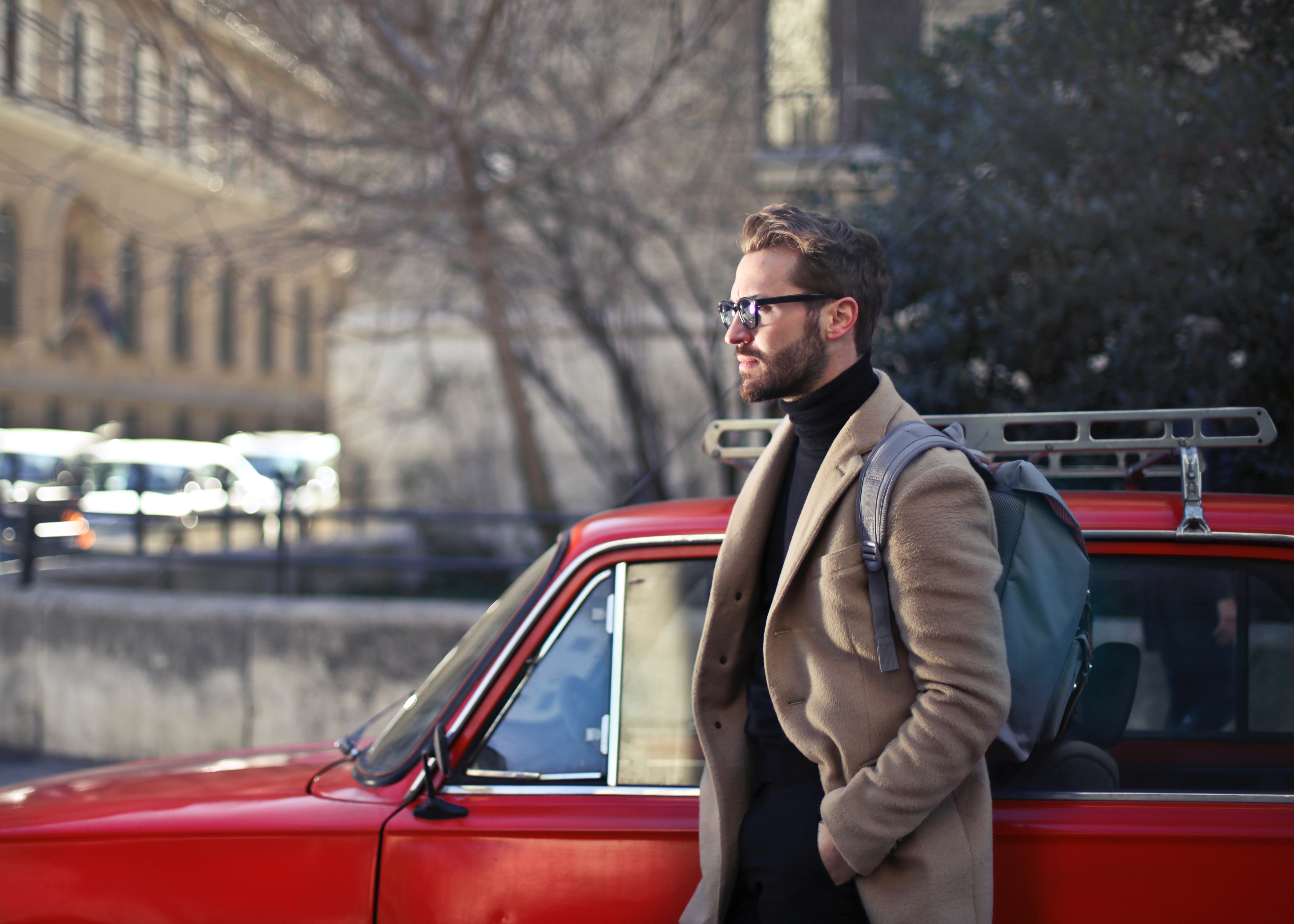 Man wearing beige jacket beside red car photo