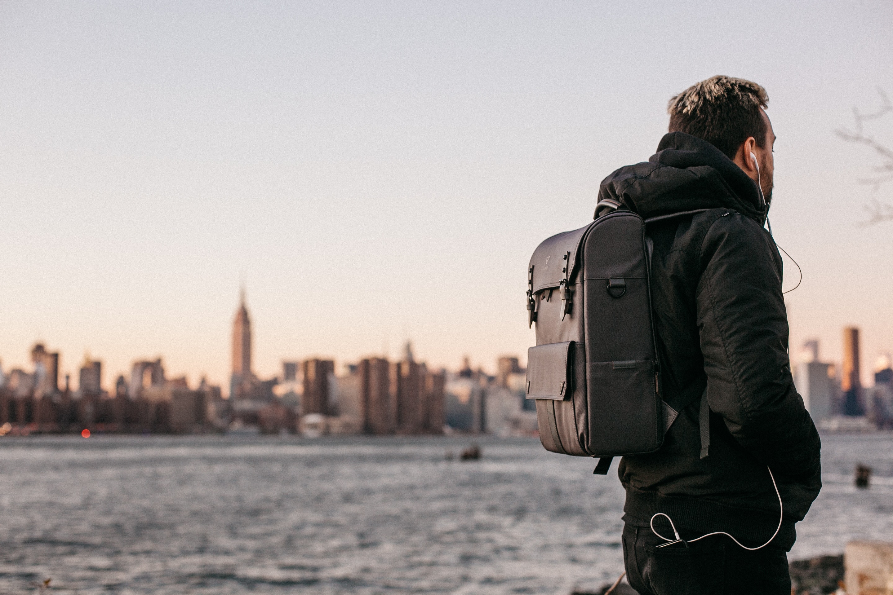 Man Wearing Black Bubble Jacket and Black Leather Backpack Near Bay, Architecture, Landscape, Tower, Skyscrapers, HQ Photo