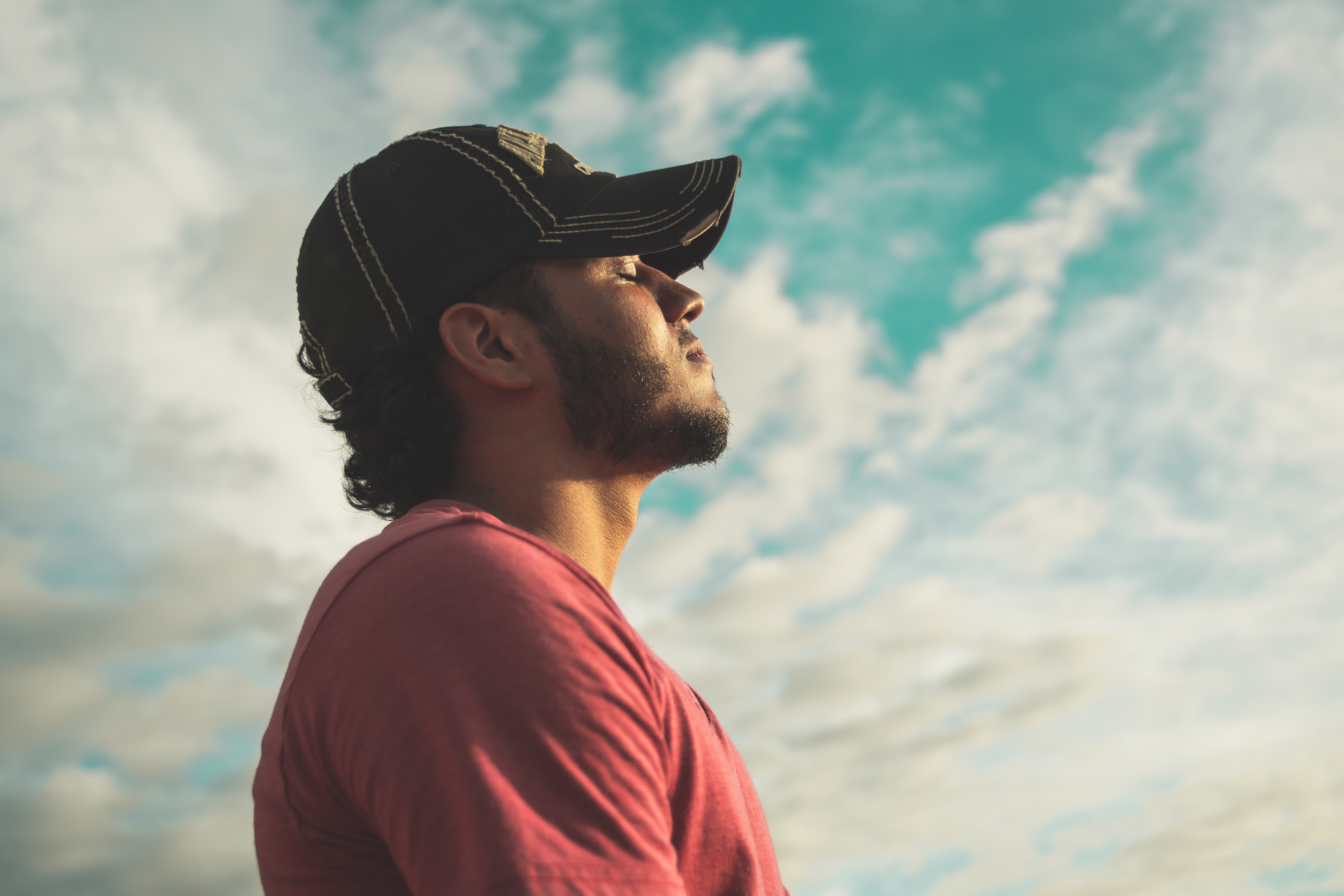Man wearing black cap with eyes closed under cloudy sky photo