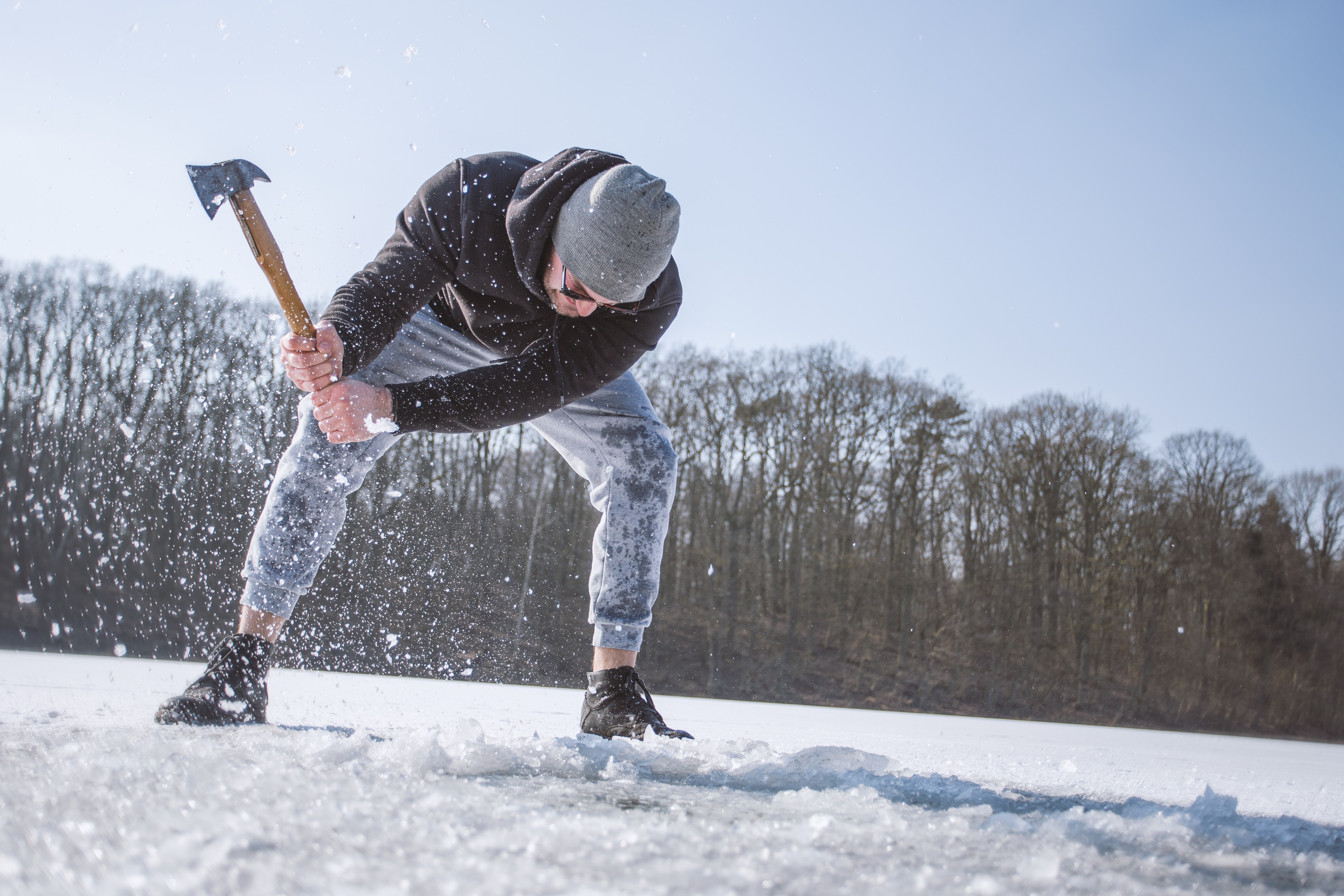 Man Wearing Black Hooded Jacket, Gray Knit Cap, Gray Pants, and Black Shoes Holding Brown Handled Axe While Bending on Snow, Action, Motion, Work, Winter, HQ Photo
