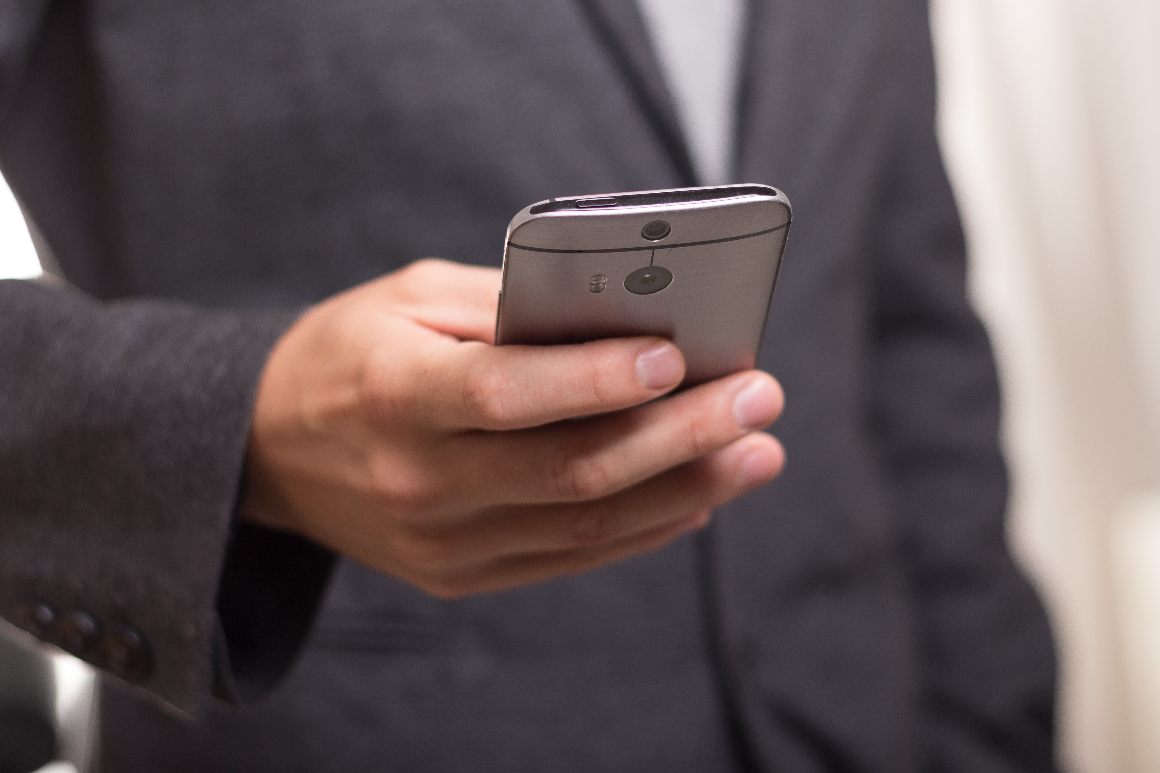 Man wearing black suit jacket holding gray htc android smartphone photo