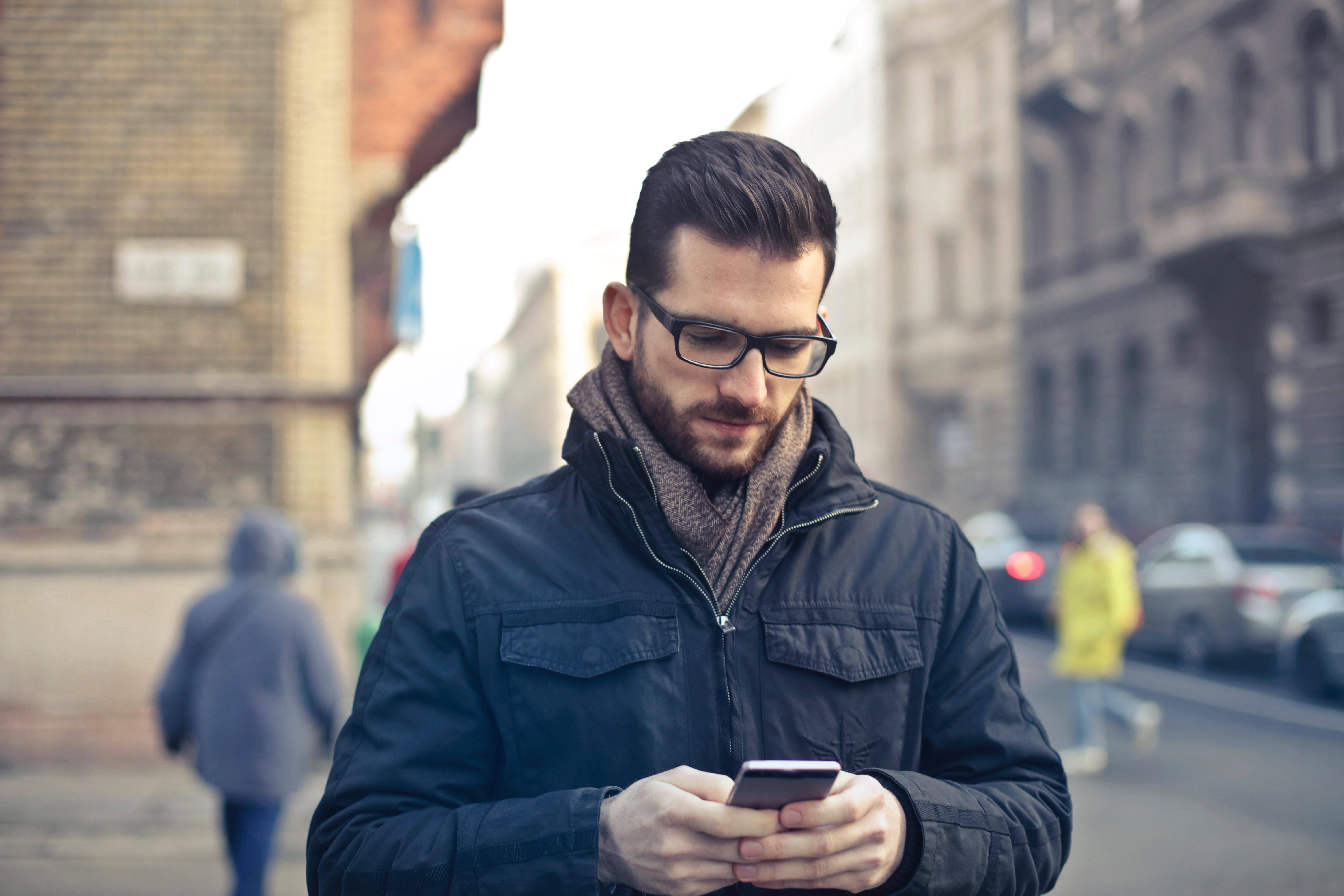 Man Wearing Black Zip Jacket Holding Smartphone Surrounded by Grey Concrete Buildings, Beard, Mobile phone, Wear, Urban, HQ Photo