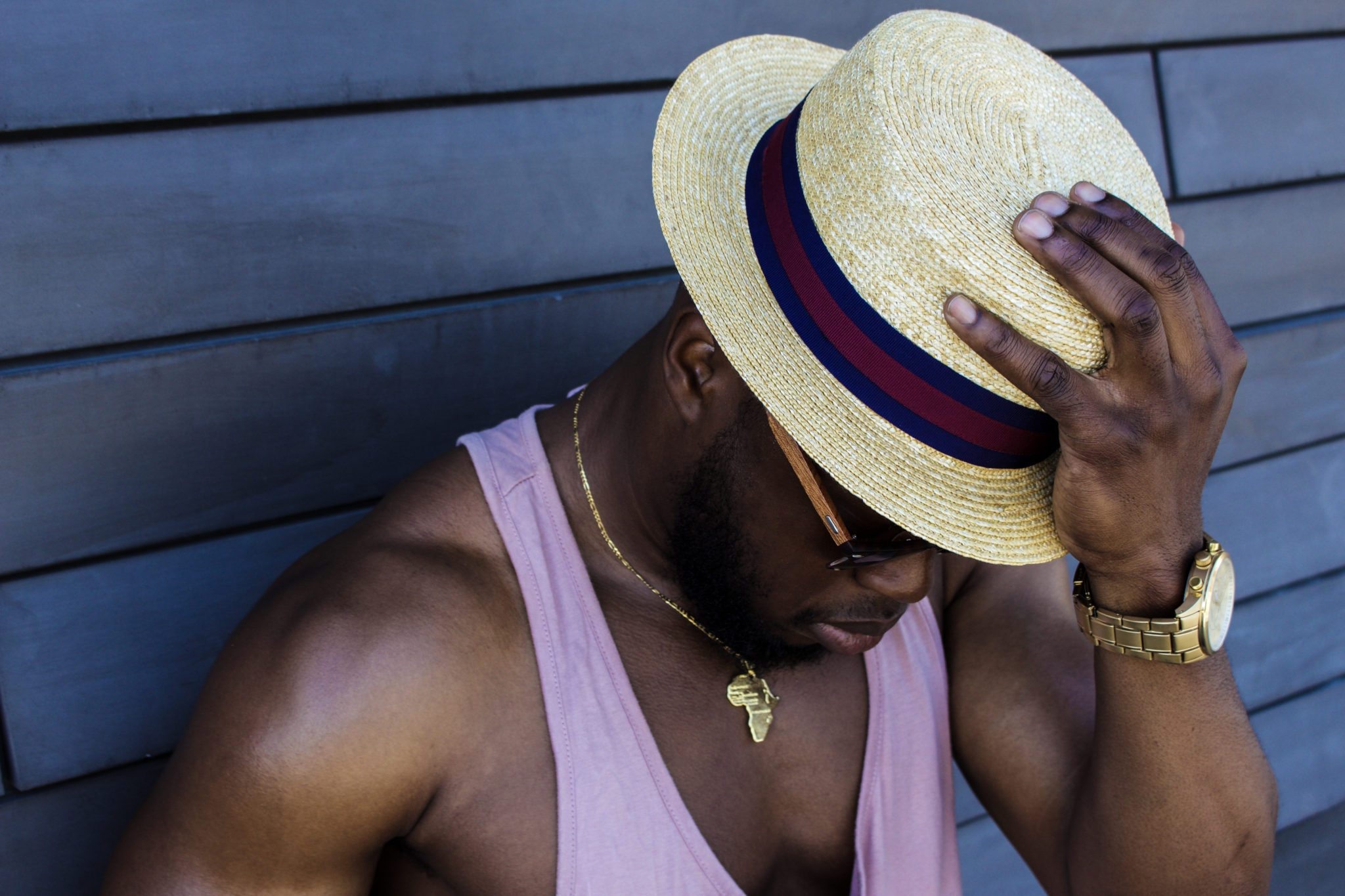 Man wearing purple tank top, gold-colored necklace, gold-colored watch, sunglasses, and beige fedora hat outfit photo
