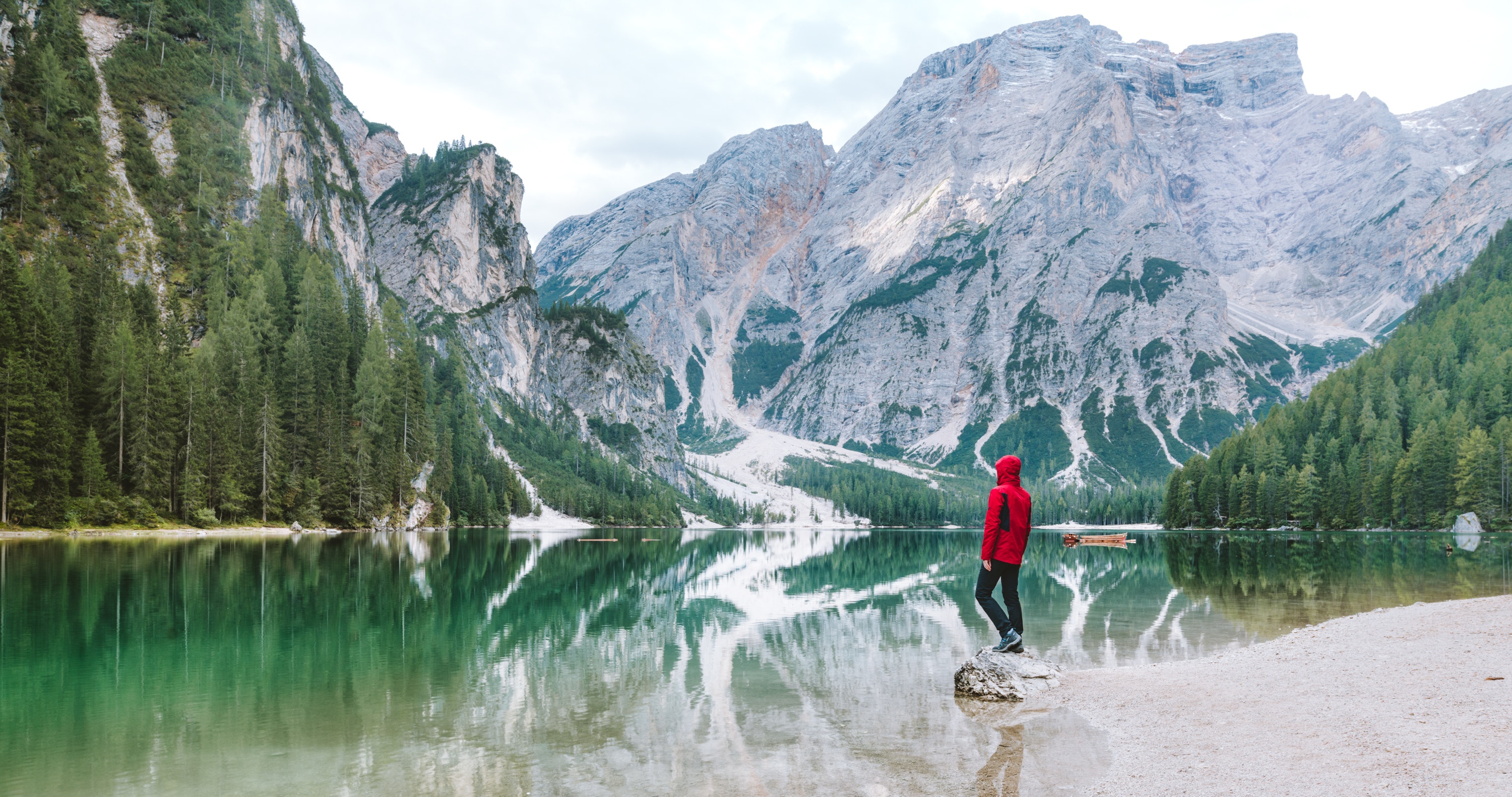 Man wearing red hoodie standing near body of water with view of mountains photo