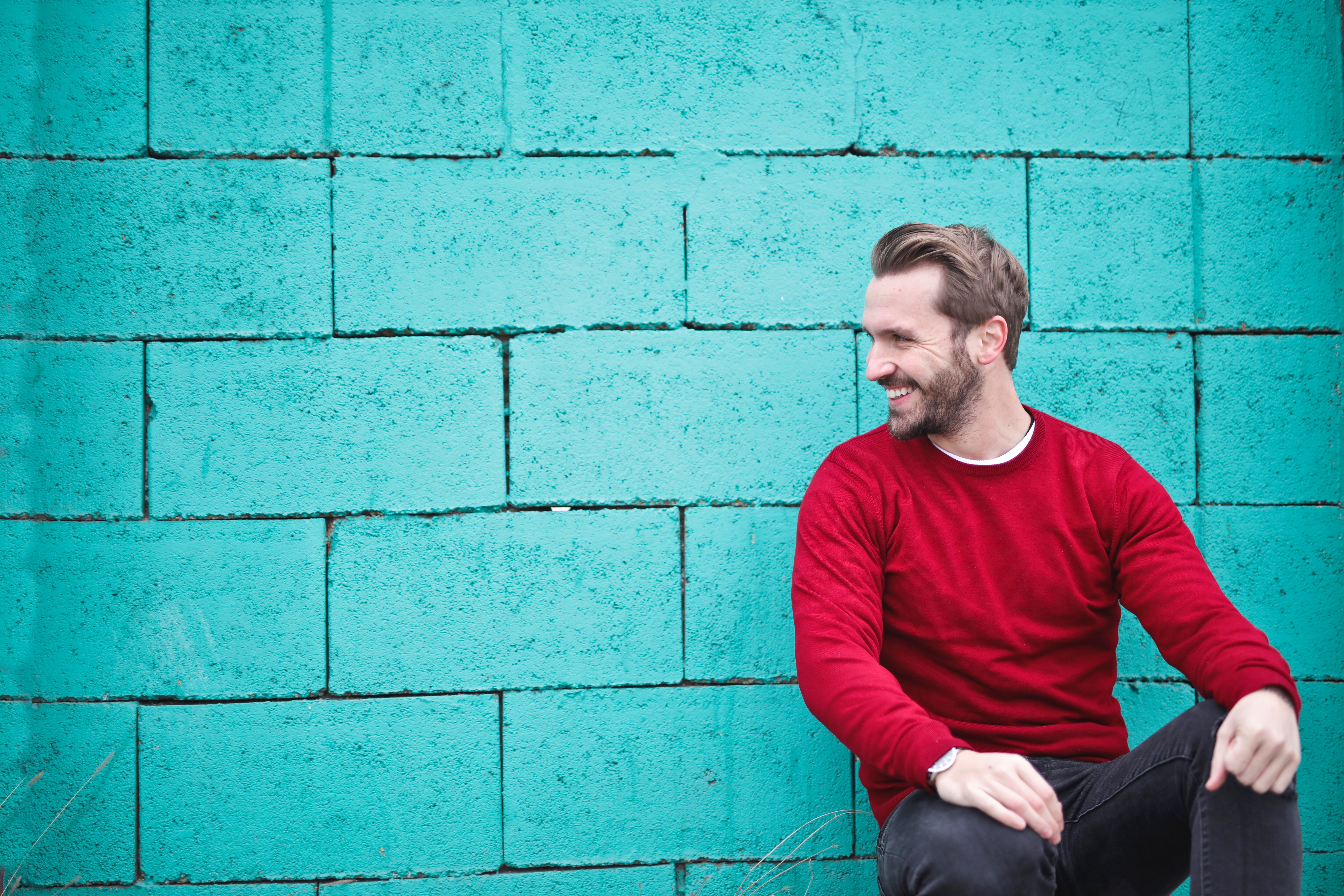 Man wearing red sweatshirt and black pants leaning on the wall photo