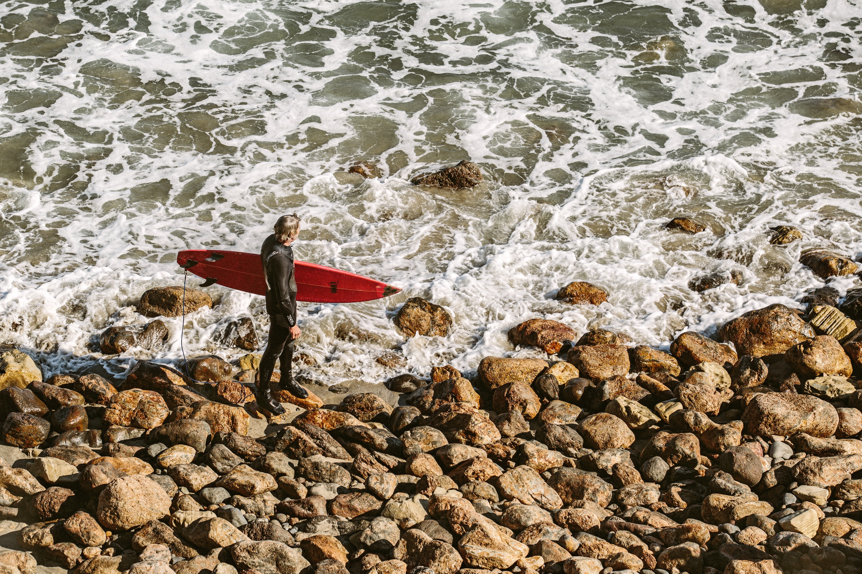 Man wearing wetsuit and holding red surfboard on shore photo