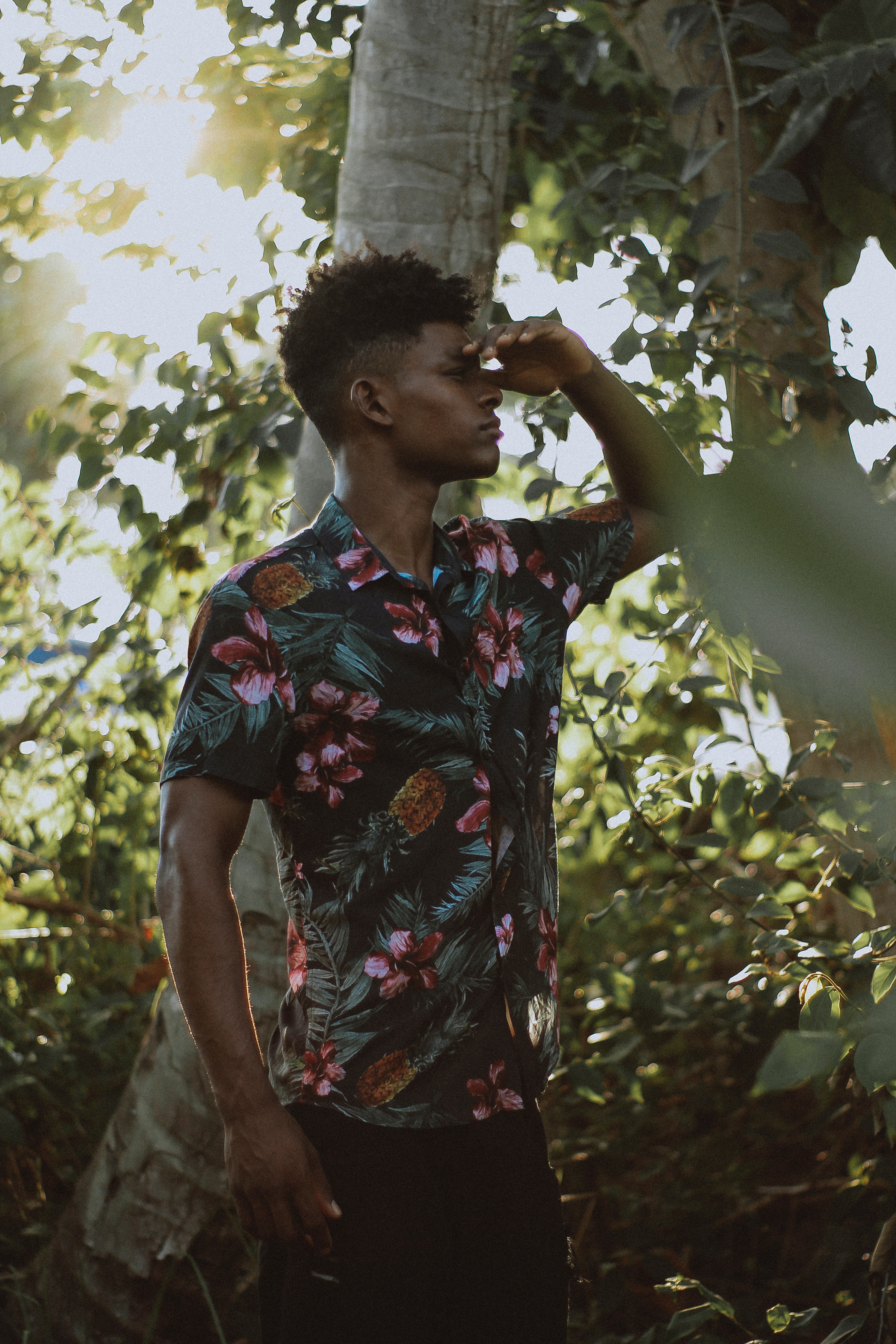 Man wears multicolored floral button-up short-sleeved shirt beside tree photo