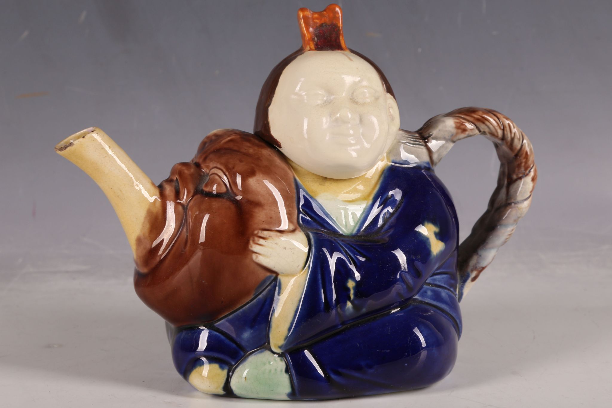 A novelty majolica teapot, modelled as a Chinese man holding a large ...