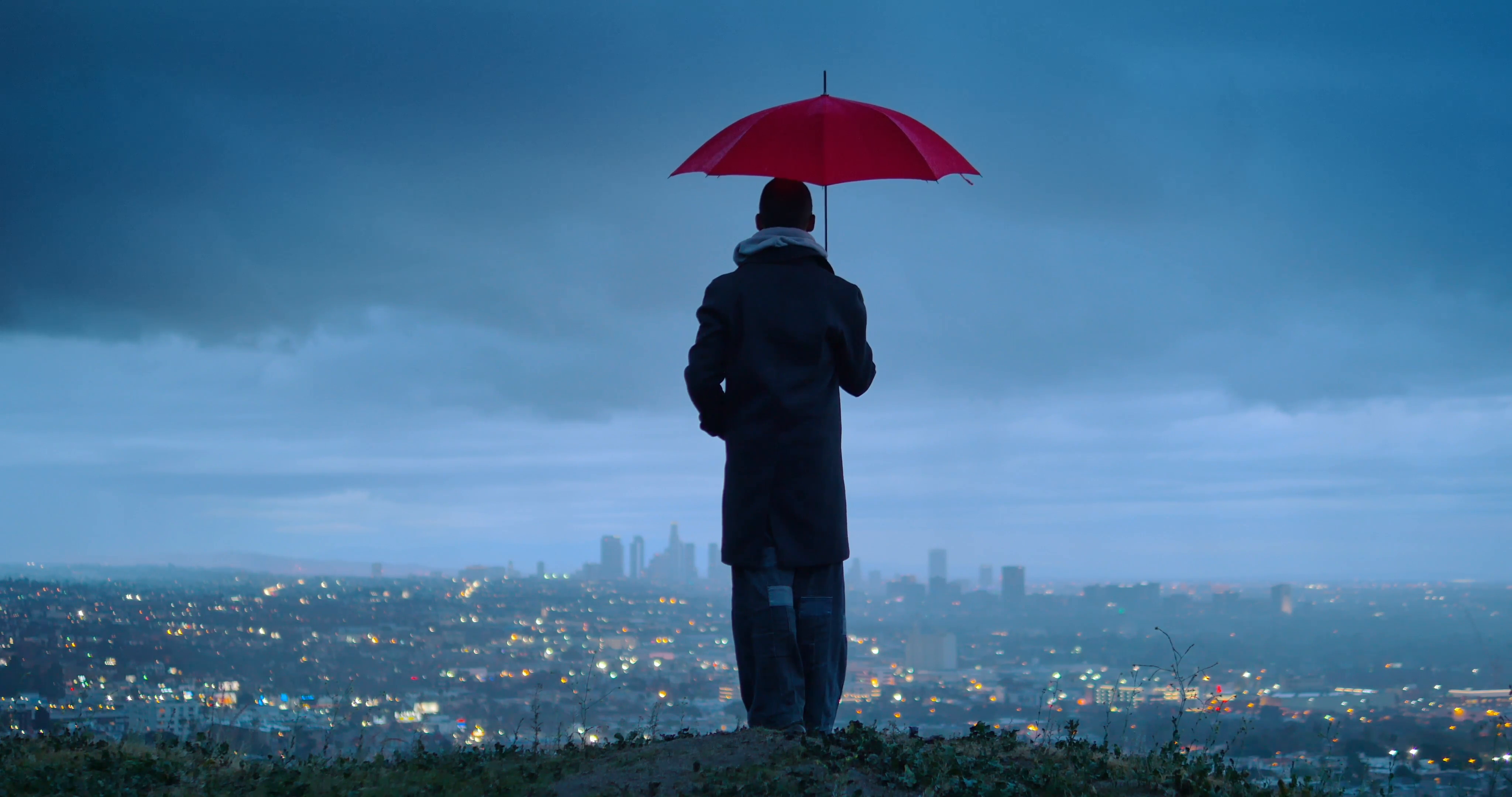 Man under red umbrella overlooking Los Angeles cityscape from ...