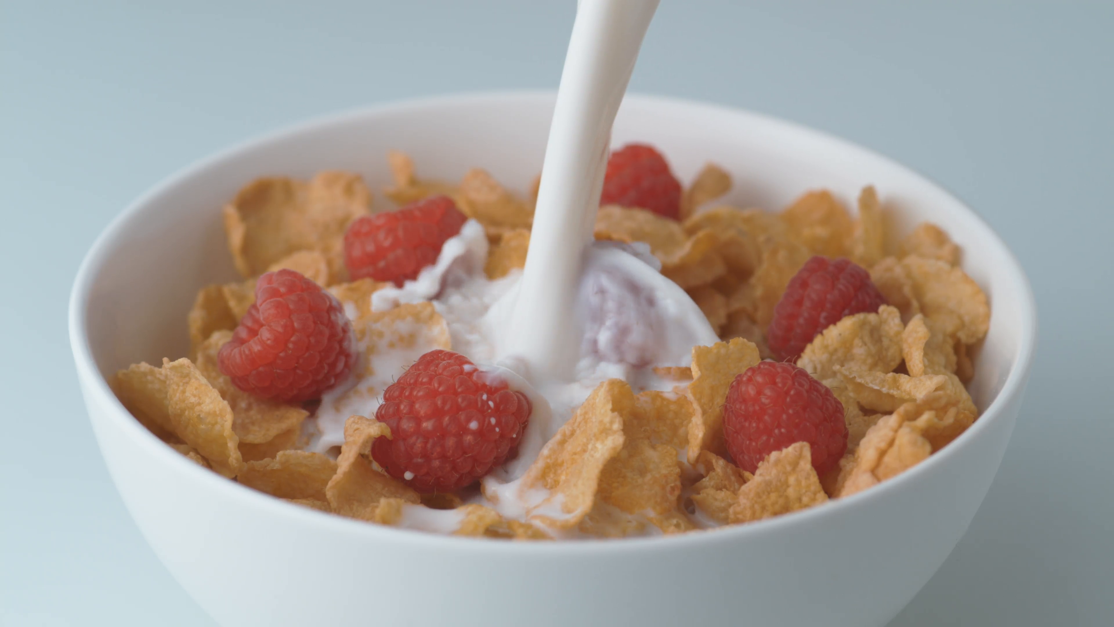 Corn flakes with raspberry in a bowl pouring with milk. Slow Motion ...