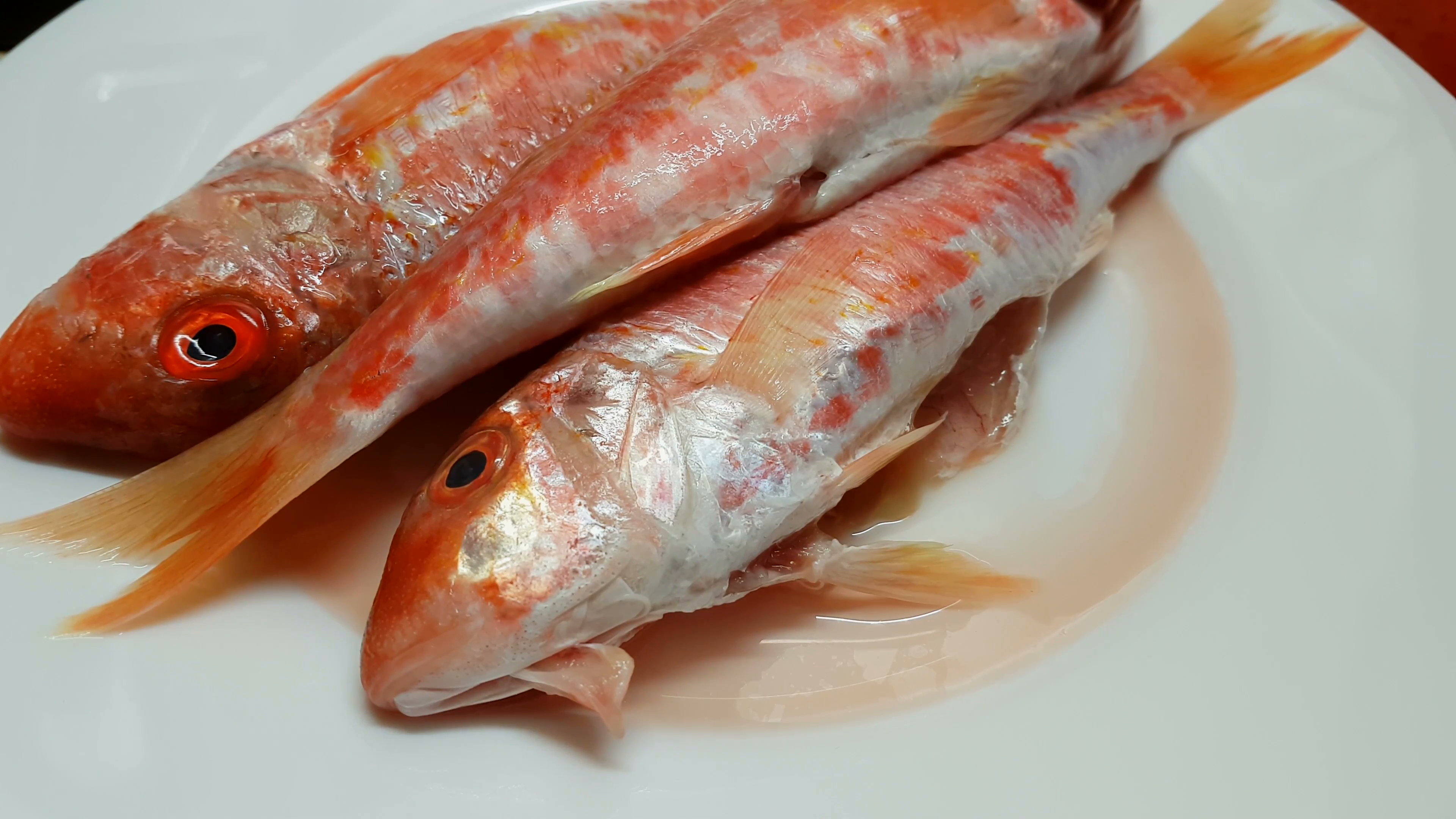 Red fresh mullets on a white plate. Raw striped red mullet fish ...