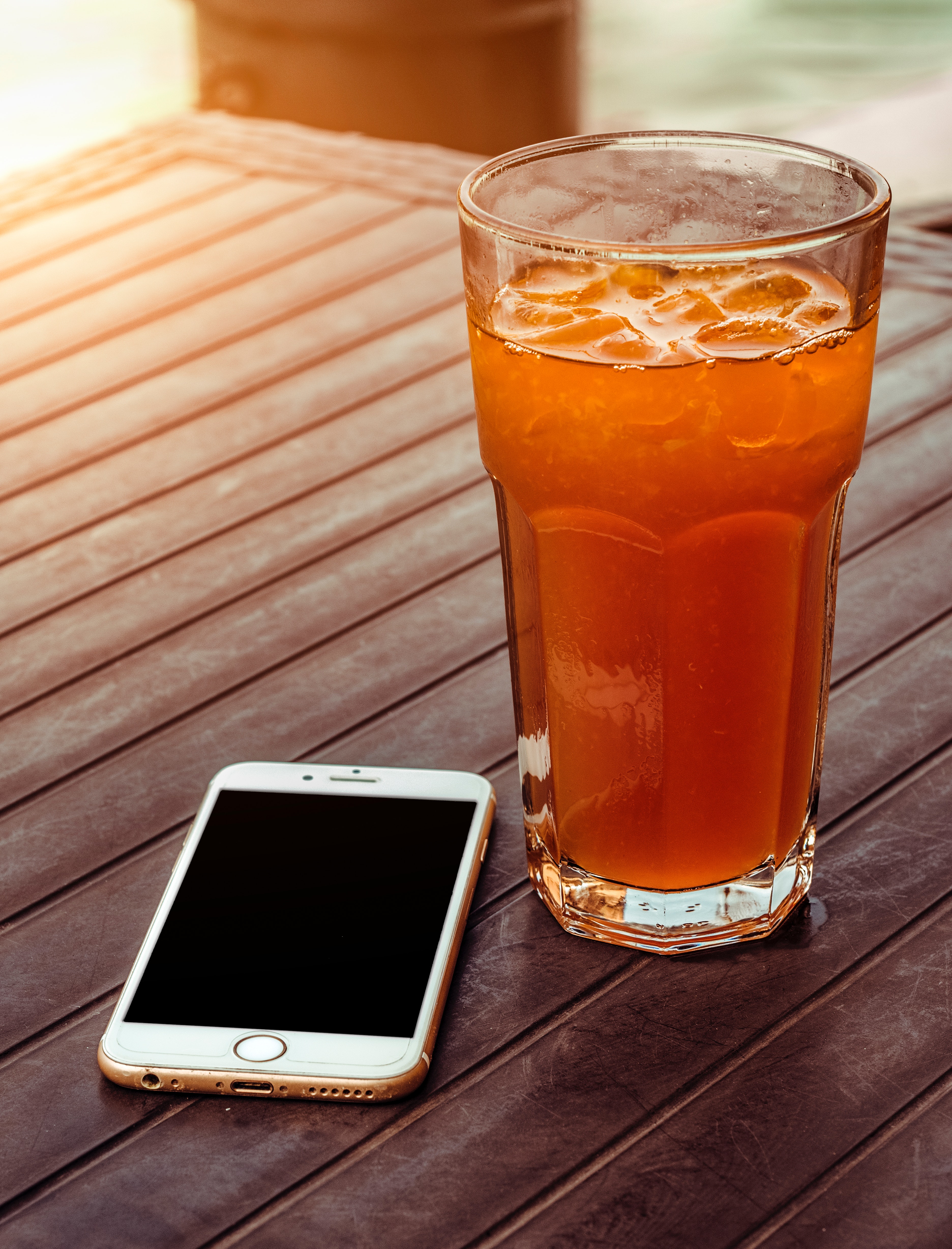 Orange juice in clear drinking glass besides gold iphone 6 on brown wooden table photo