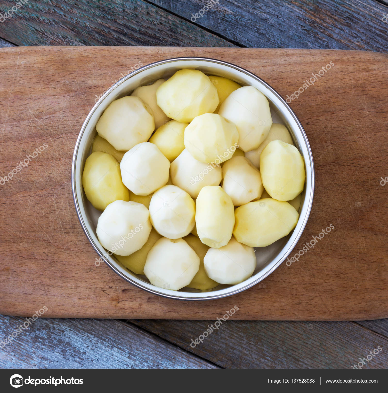 raw peeled potatoes in a circular bowl on an old cutting board on ...