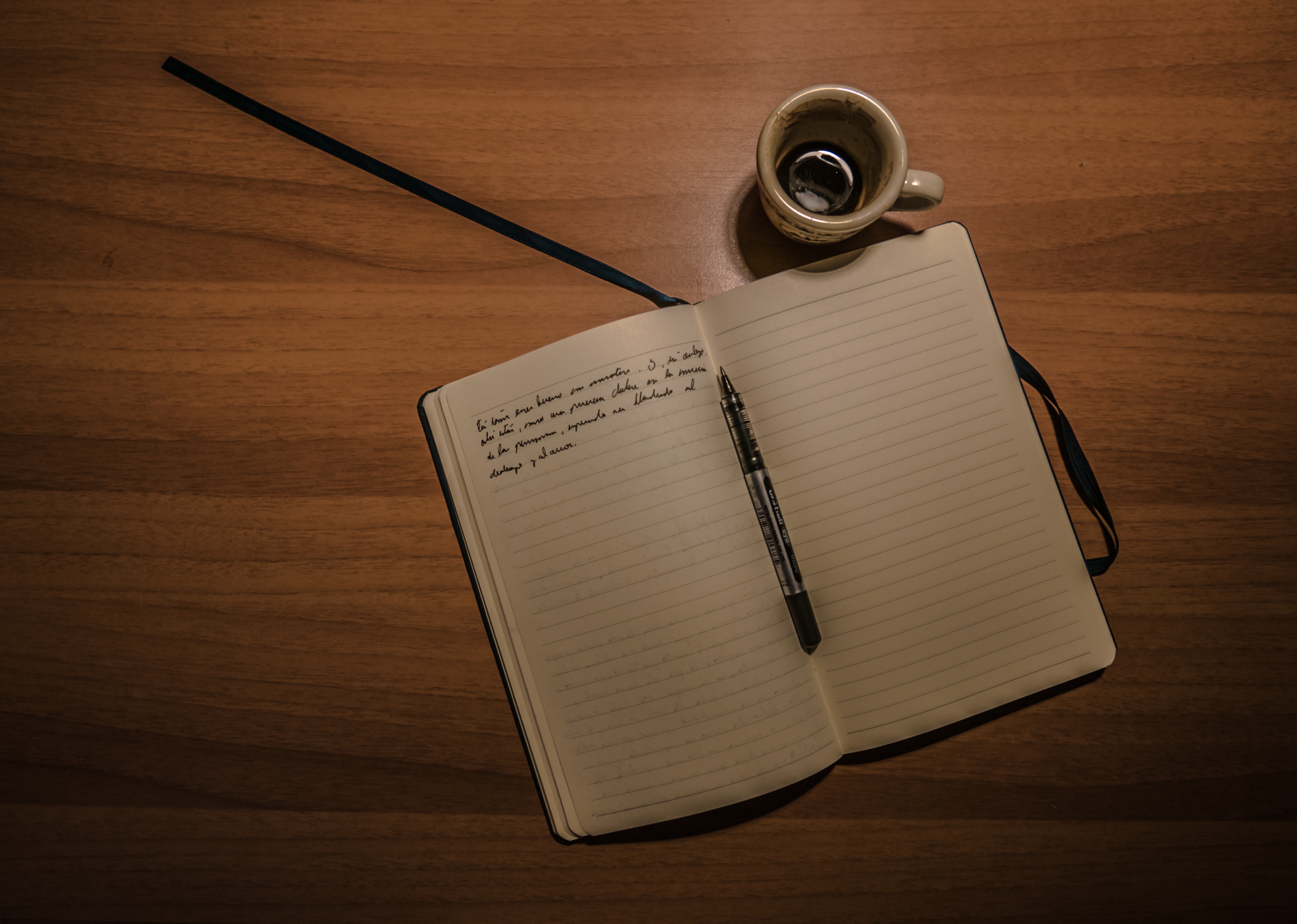 Pen on notebook beside a teacup on brown wooden plank photo