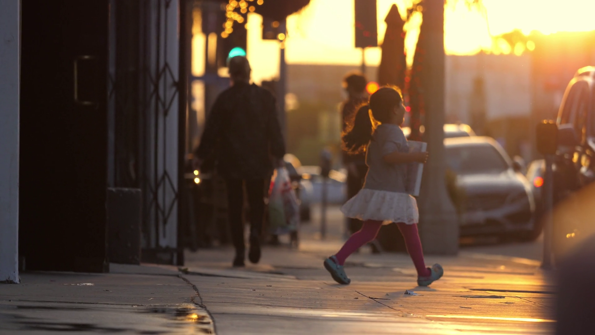 Happy little girl in city running across street sidewalk at sunset ...