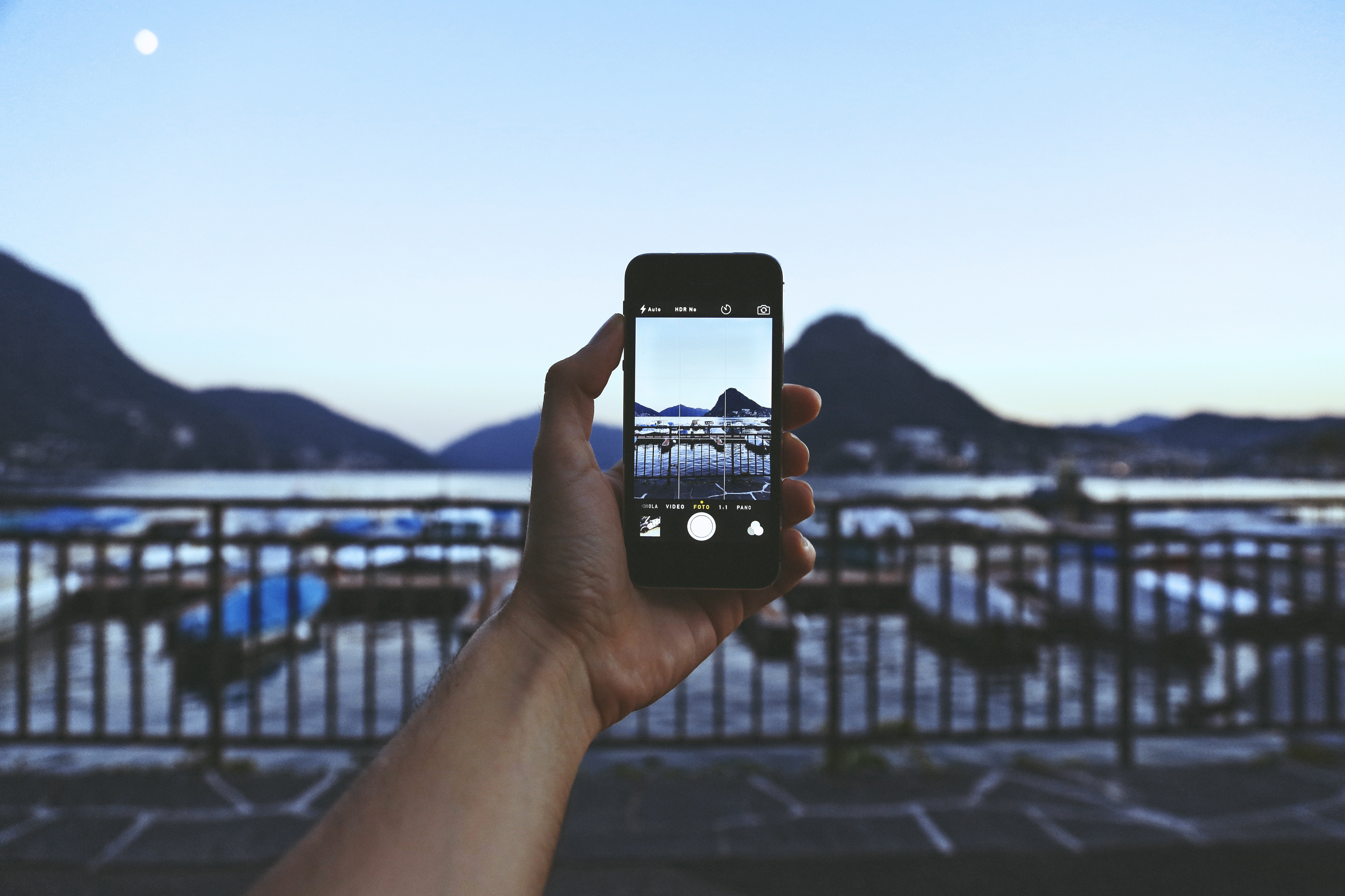Person holding iphone taking picture of mountain near body of water photo