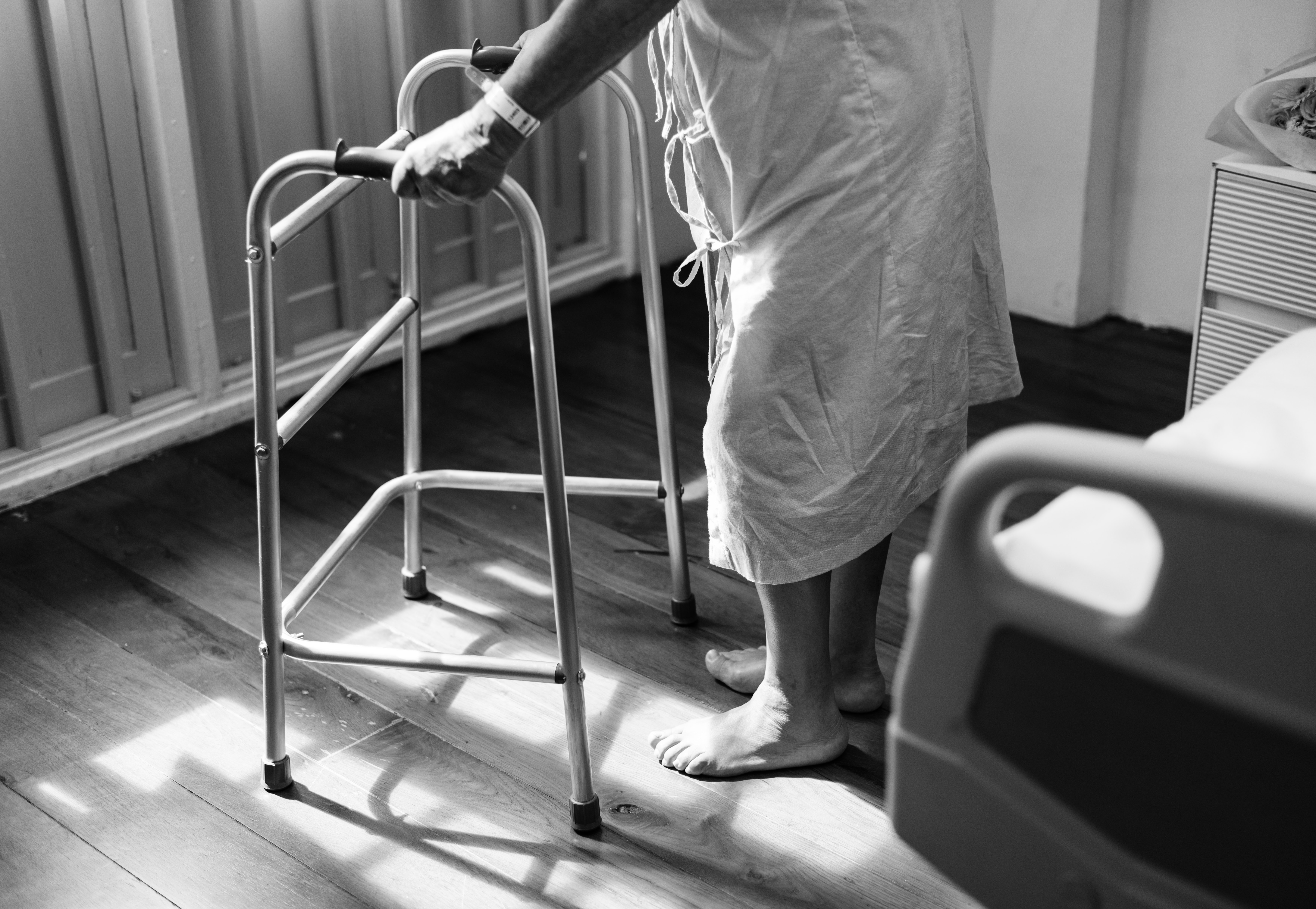 Person holding medical walker beside white hospital bed photo
