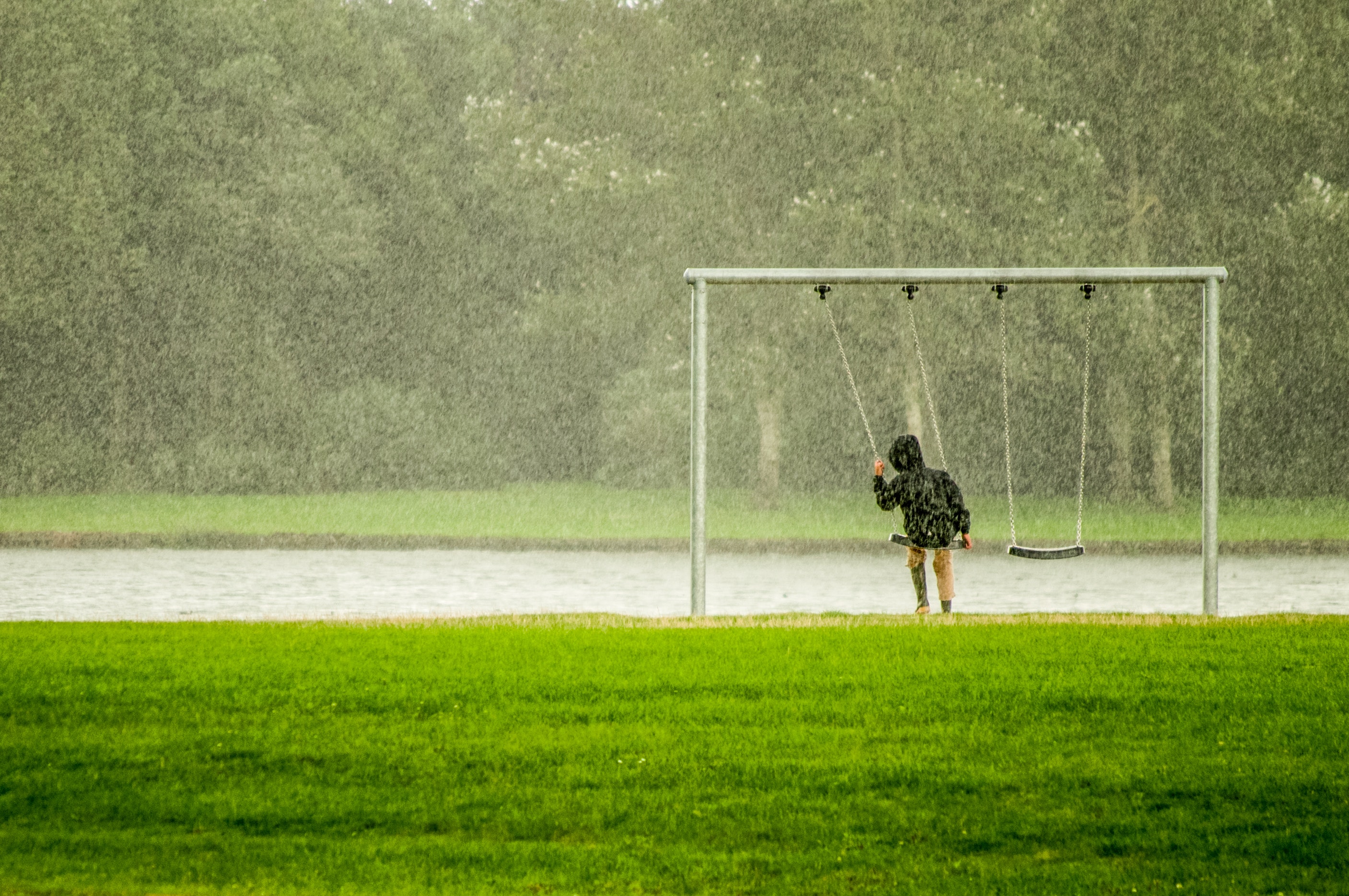 Person in black hoodie riding swing while raining photo
