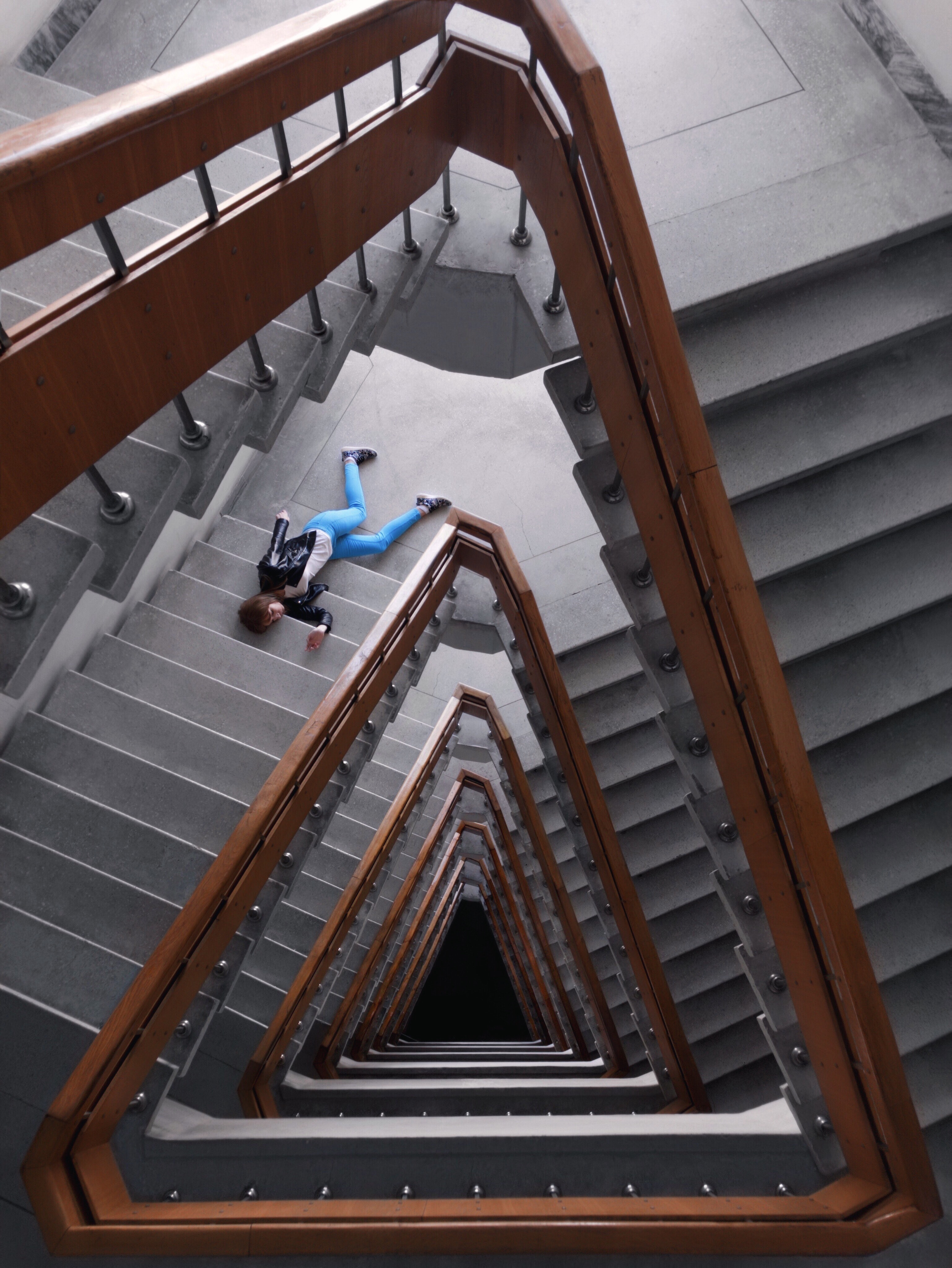 Person in black jacket and blue denim pants laying on spiral staircase photo