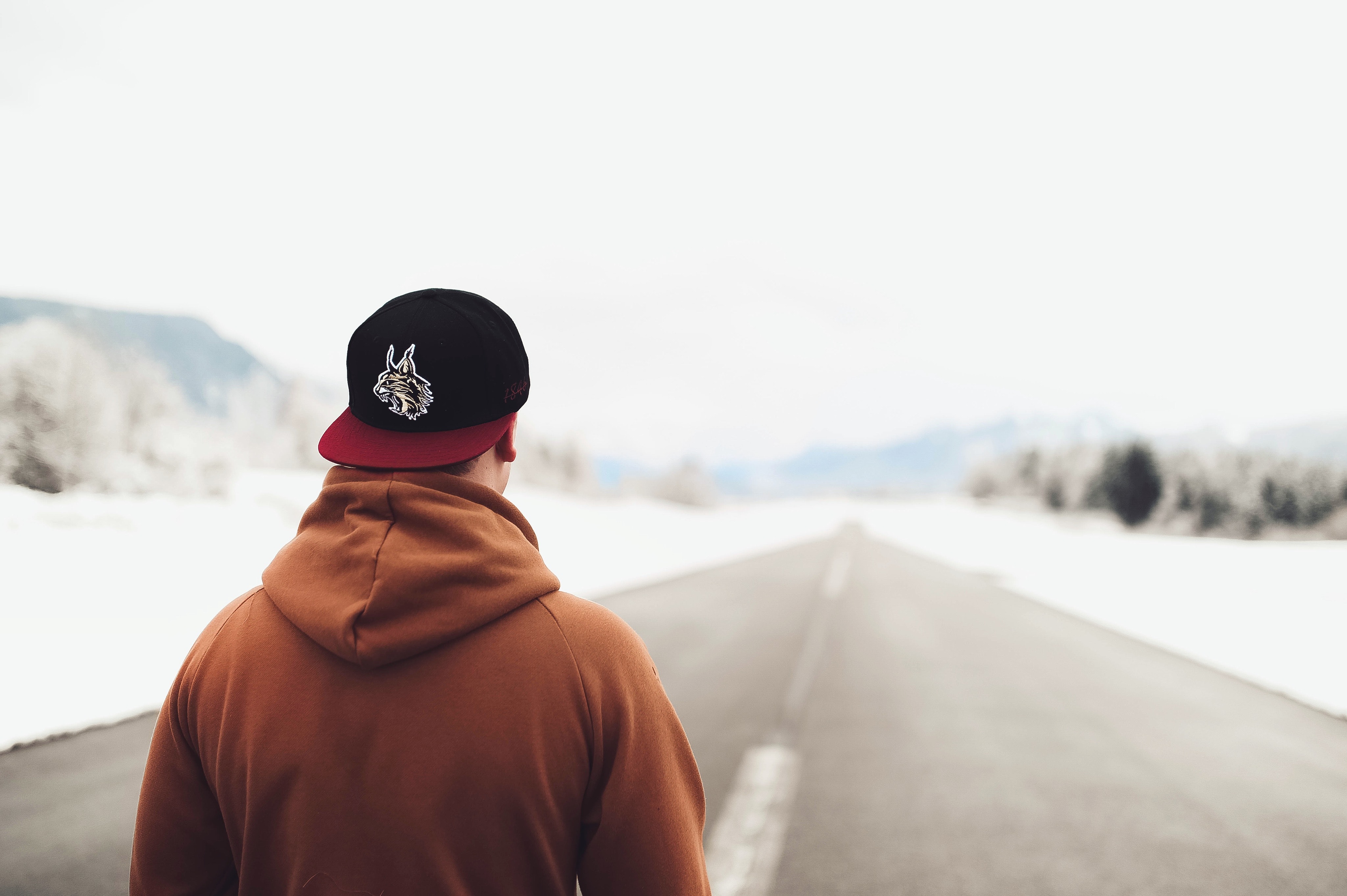 Person in brown hoodie and fitted cap walking on road photo