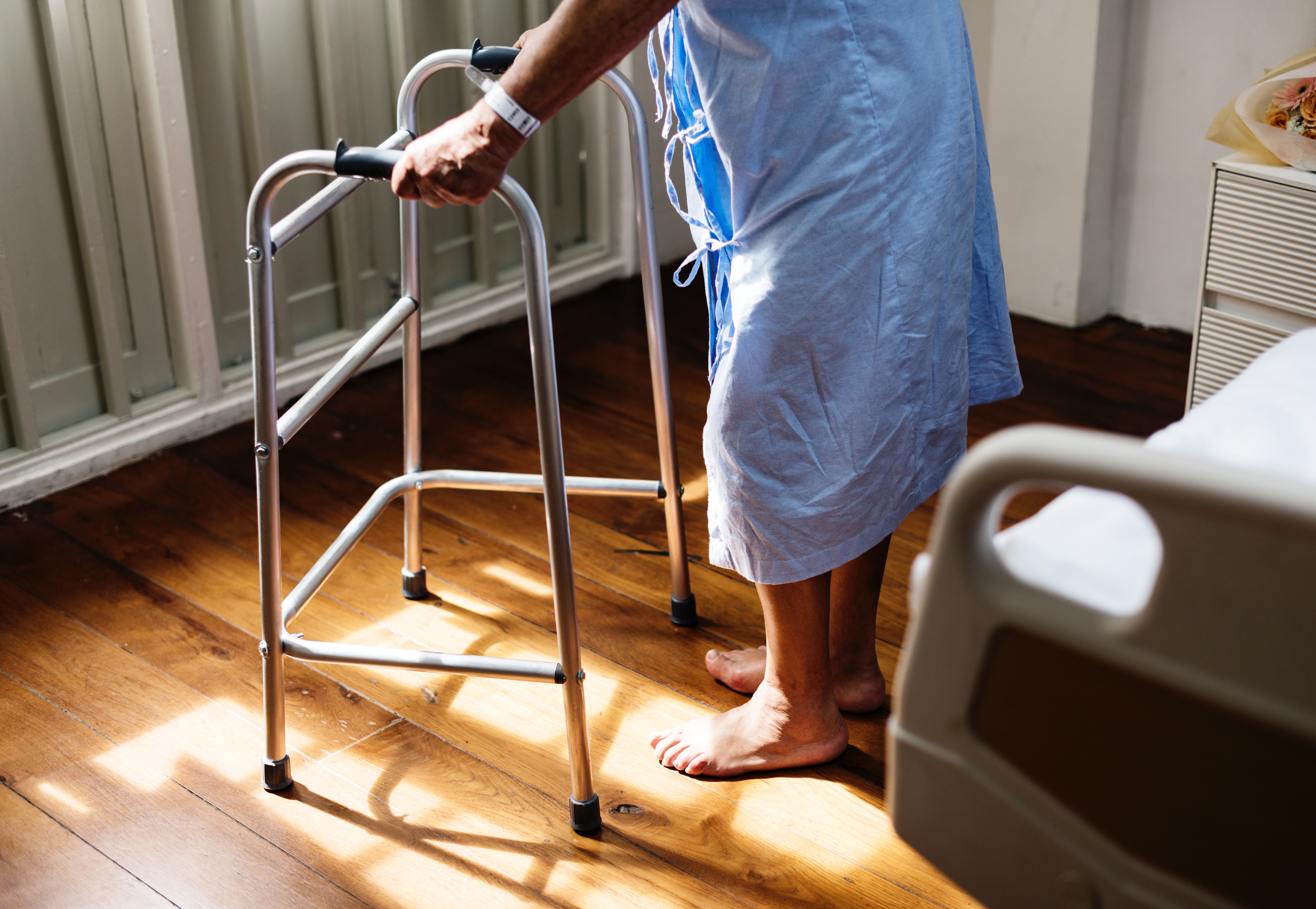 Person in hospital gown using walking frame beside hospital bed photo