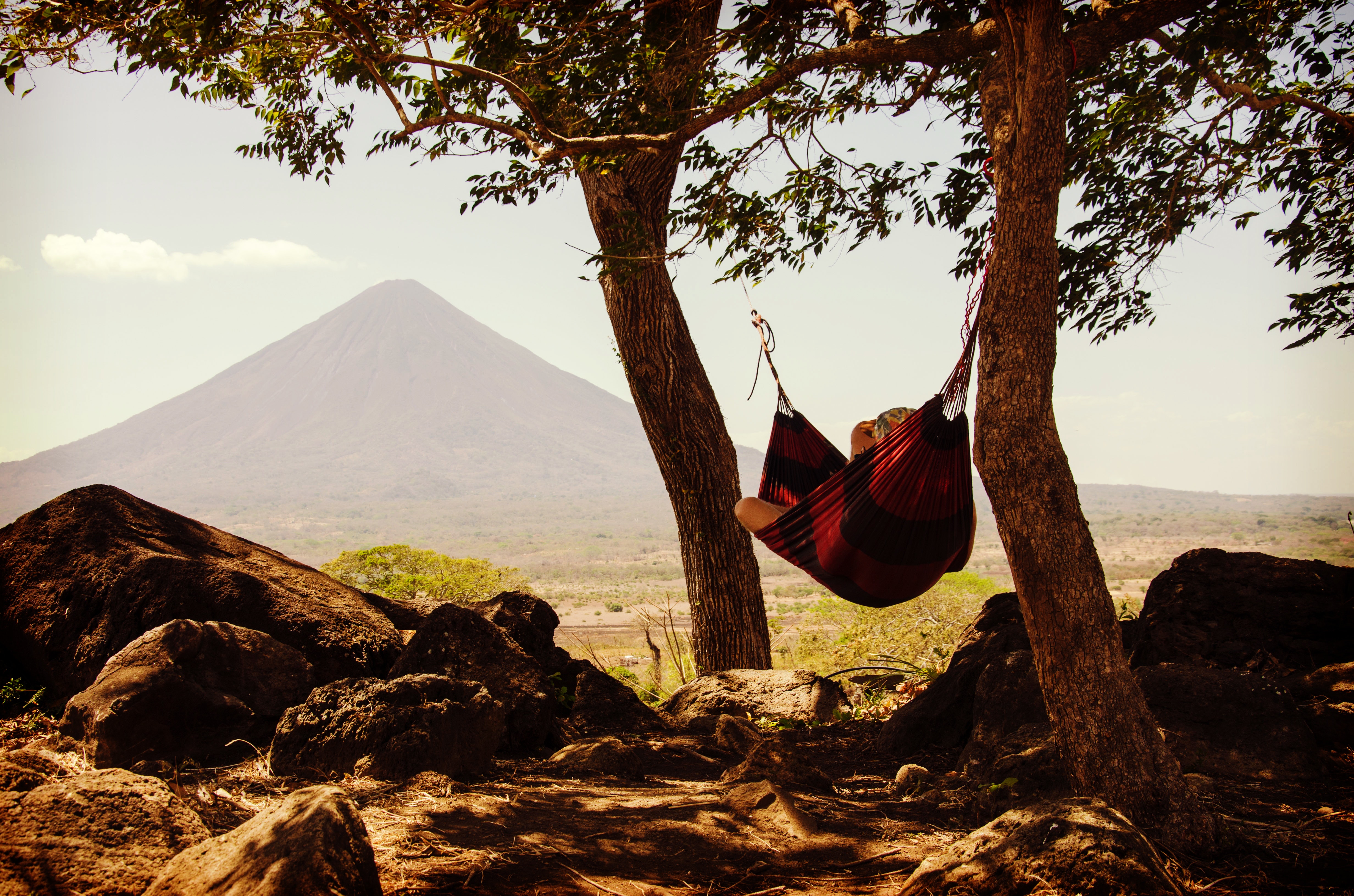 Person lying on black and red hammock beside mountain under white cloudy sky during daytime photo
