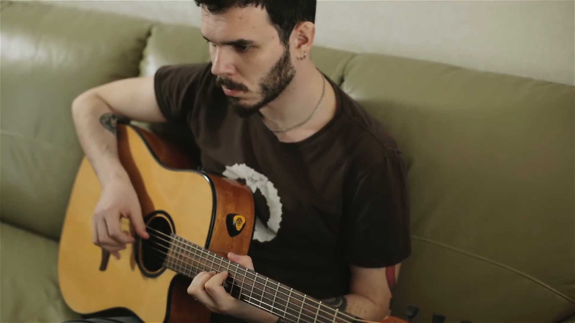 A young handsome man in a brown t-shirt playing the acoustic guitar ...