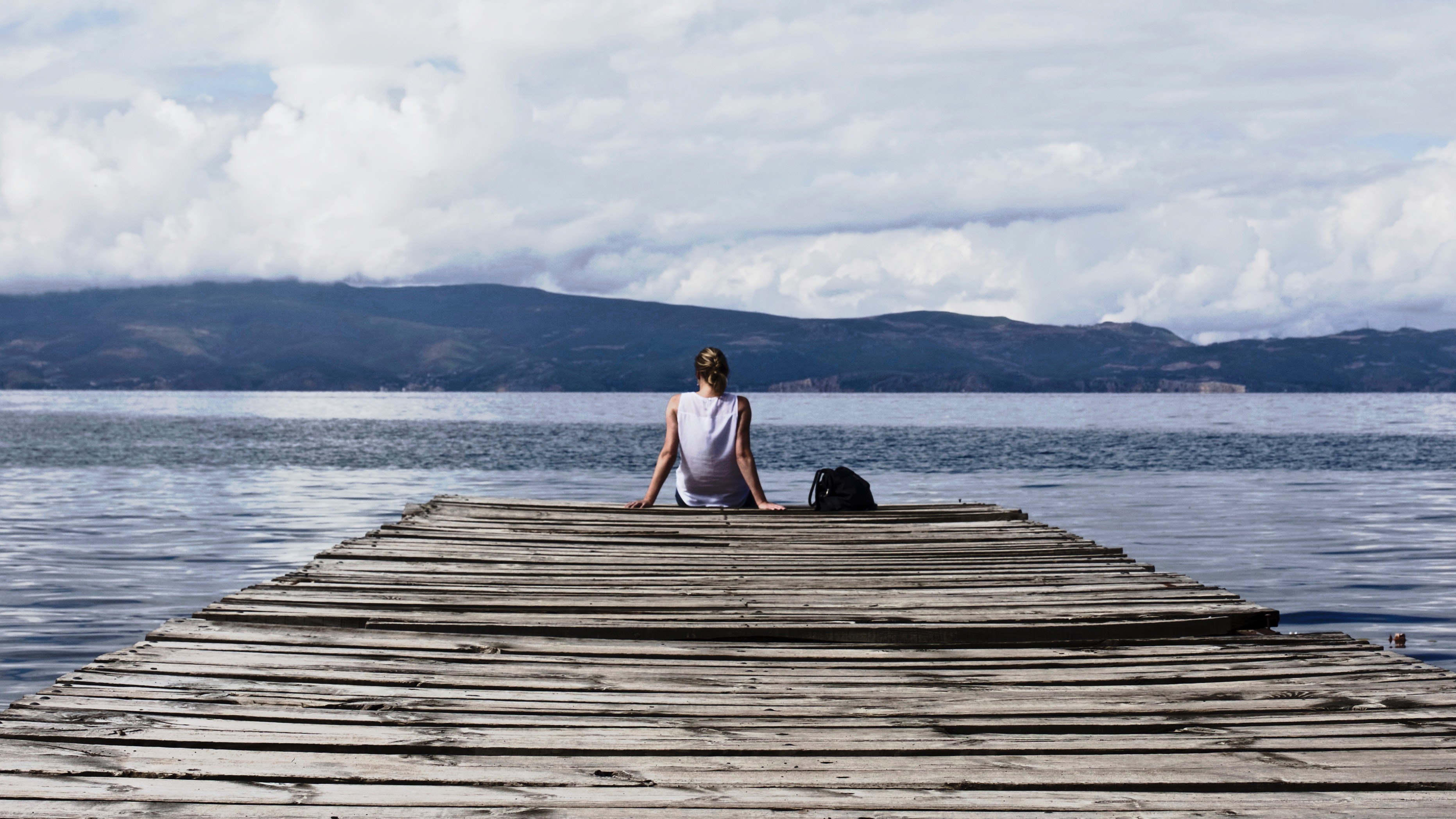 Person sitting on brown wooden dock under cloudy blue sky photo