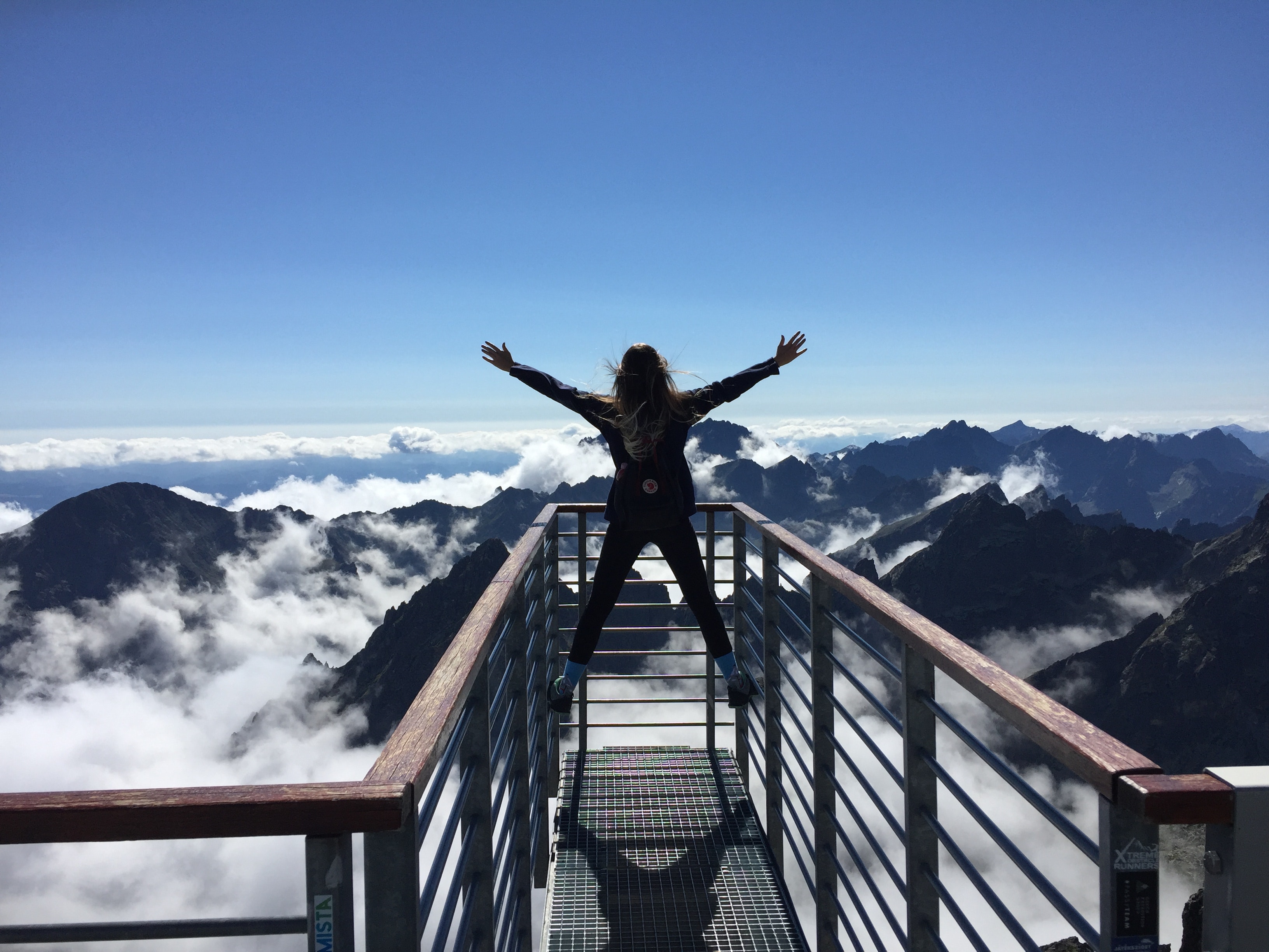 Person standing on hand rails with arms wide open facing the mountains and clouds photo