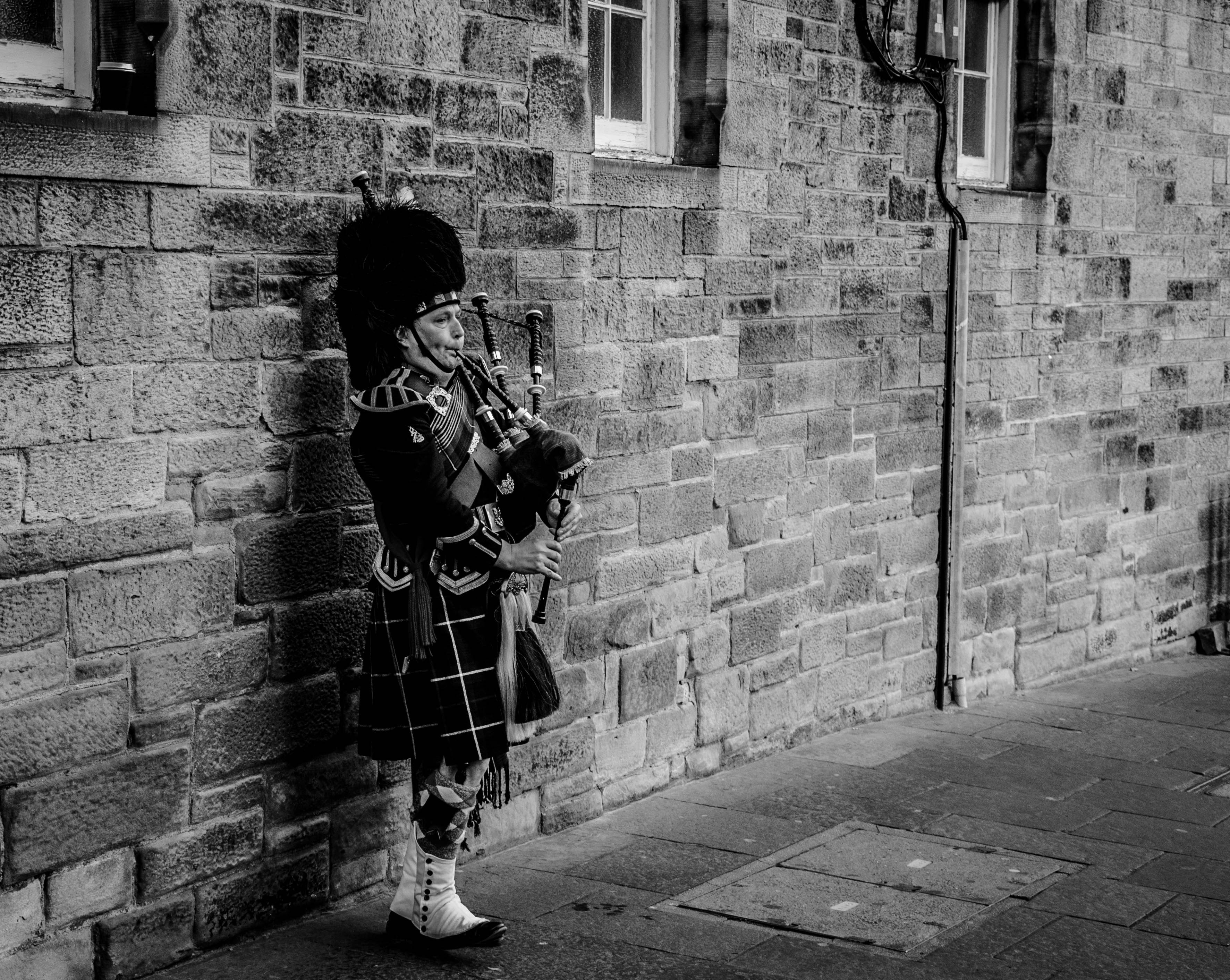 Person using bagpipes near wall in grayscale photography