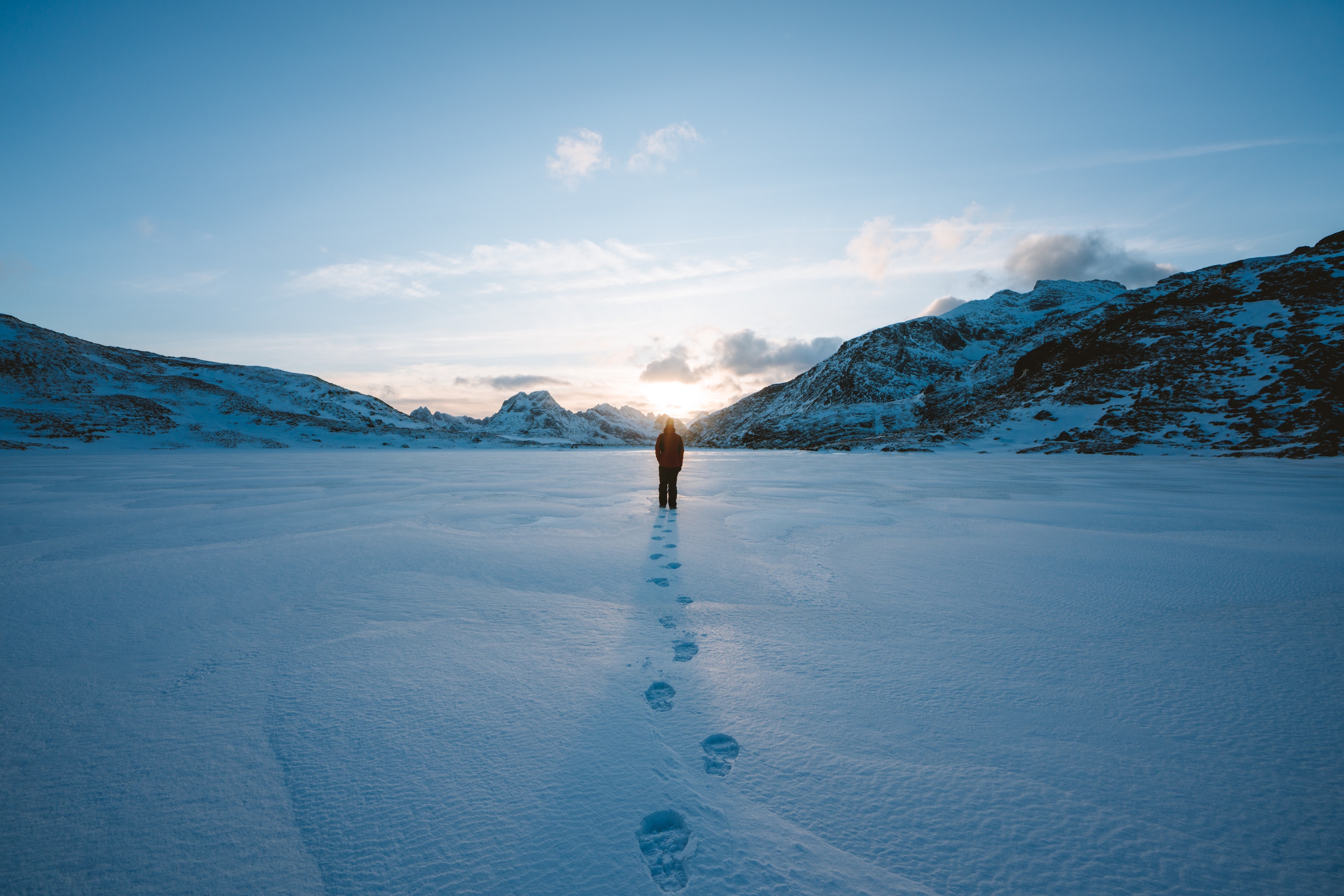 Person walking in snow field near mountain cliff covered with snow photo
