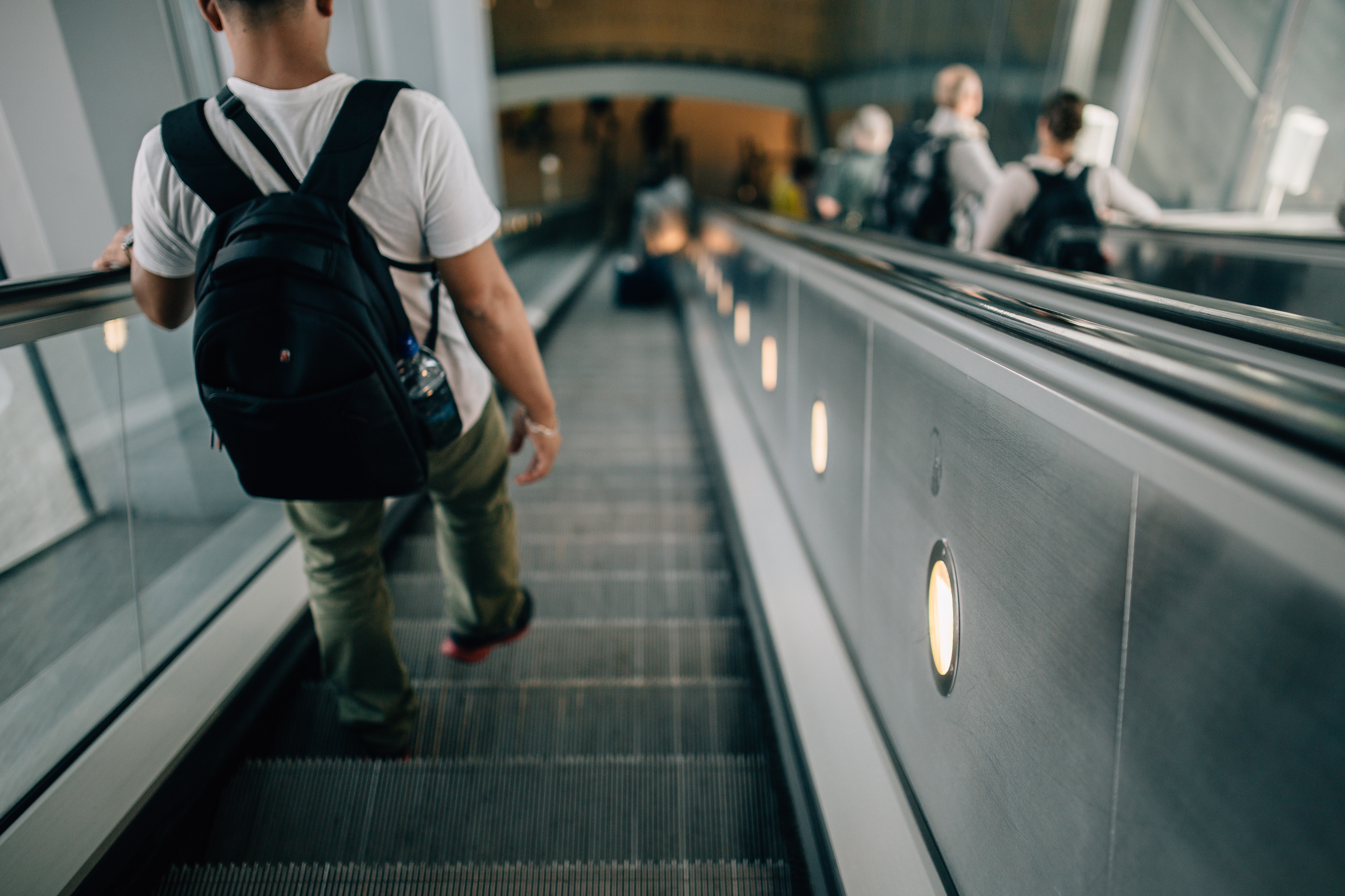 Person wearing black backpack riding down the escalator photo