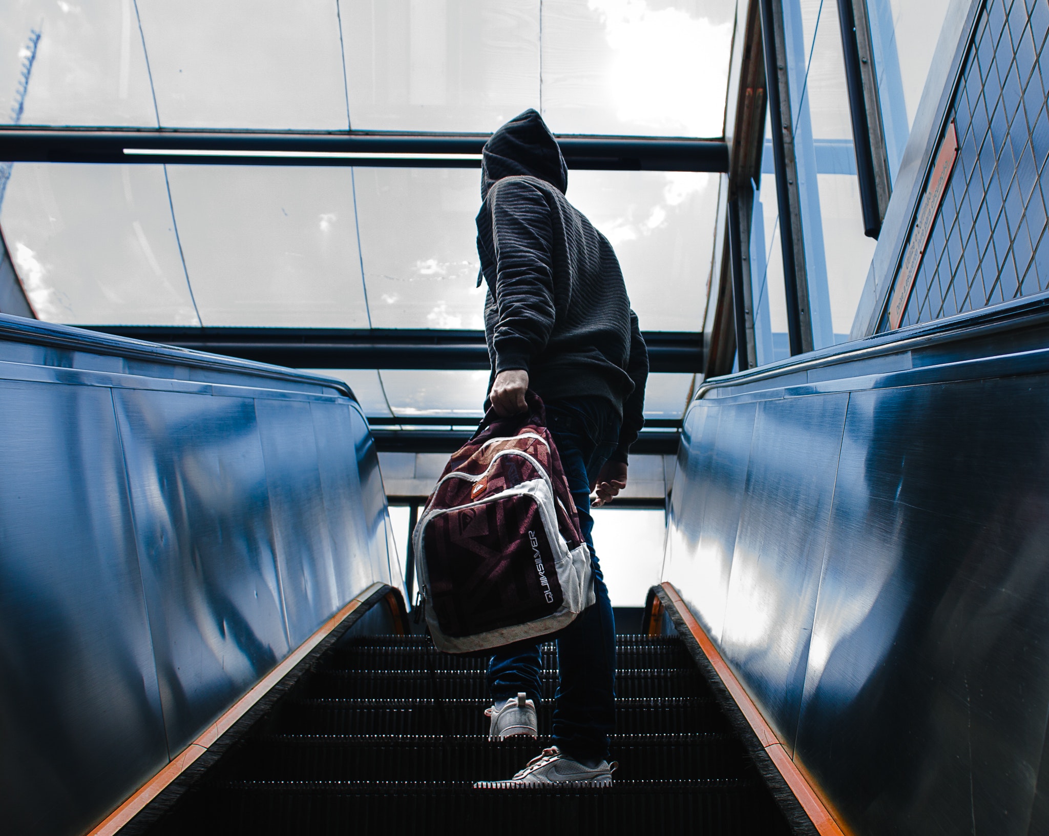 Person wearing black hooded jacket standing on escalator while holding backpack photo