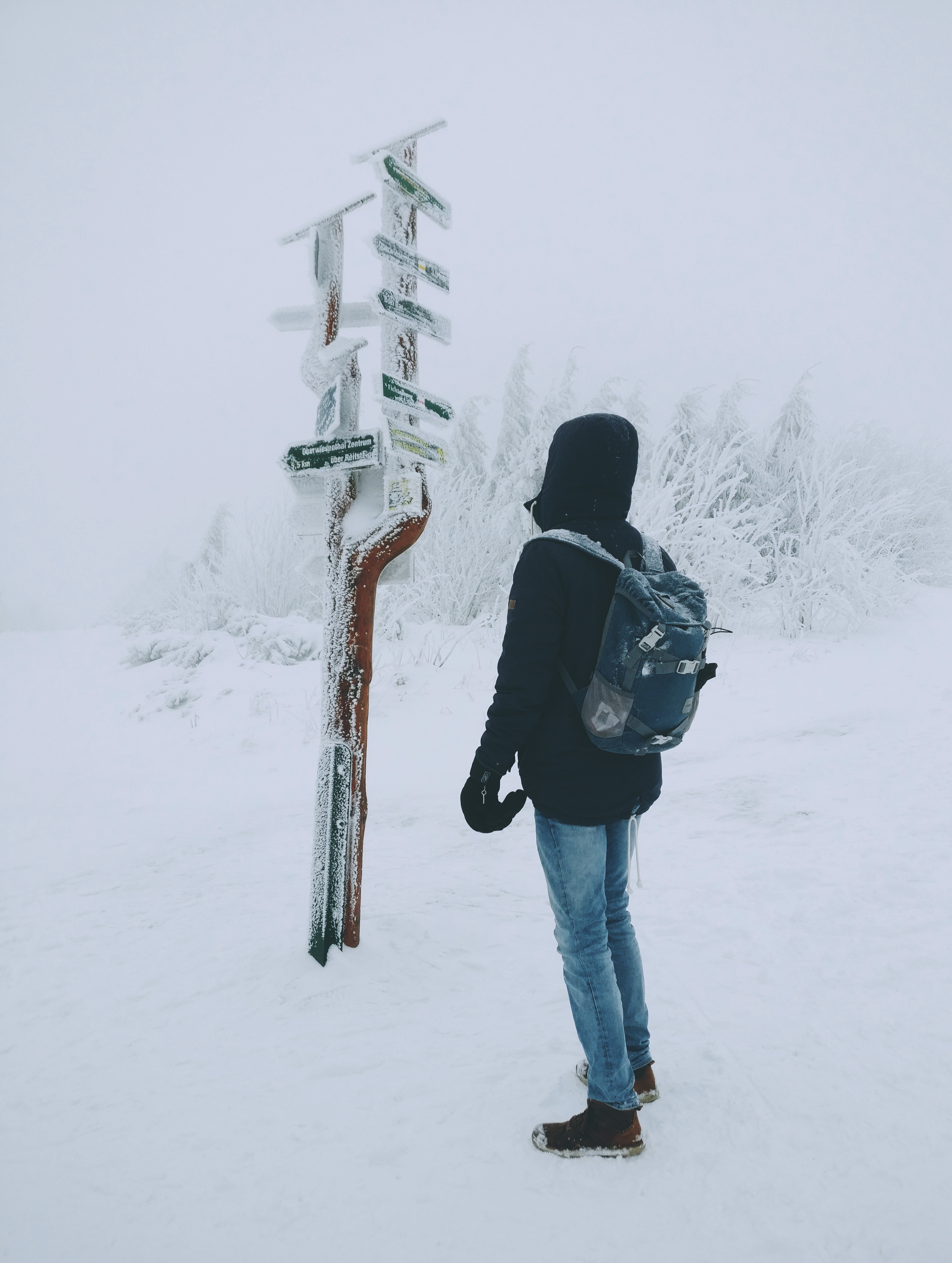 Person wearing black hoodie and blue denim jeans standing over frozen arrow signage over snow ground photo