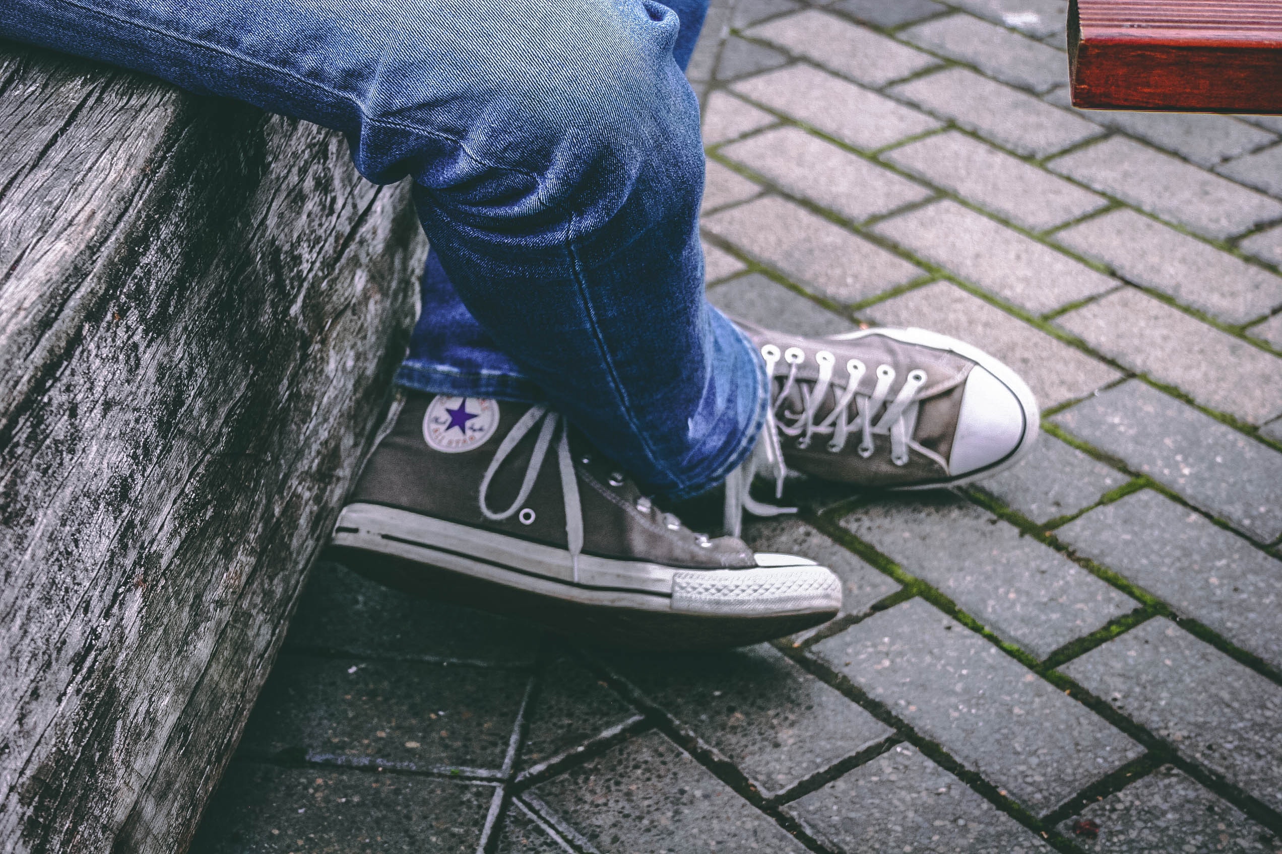 Person wearing brown converse all-star high-top sneakers and blue denim jeans while sitting on bench photo