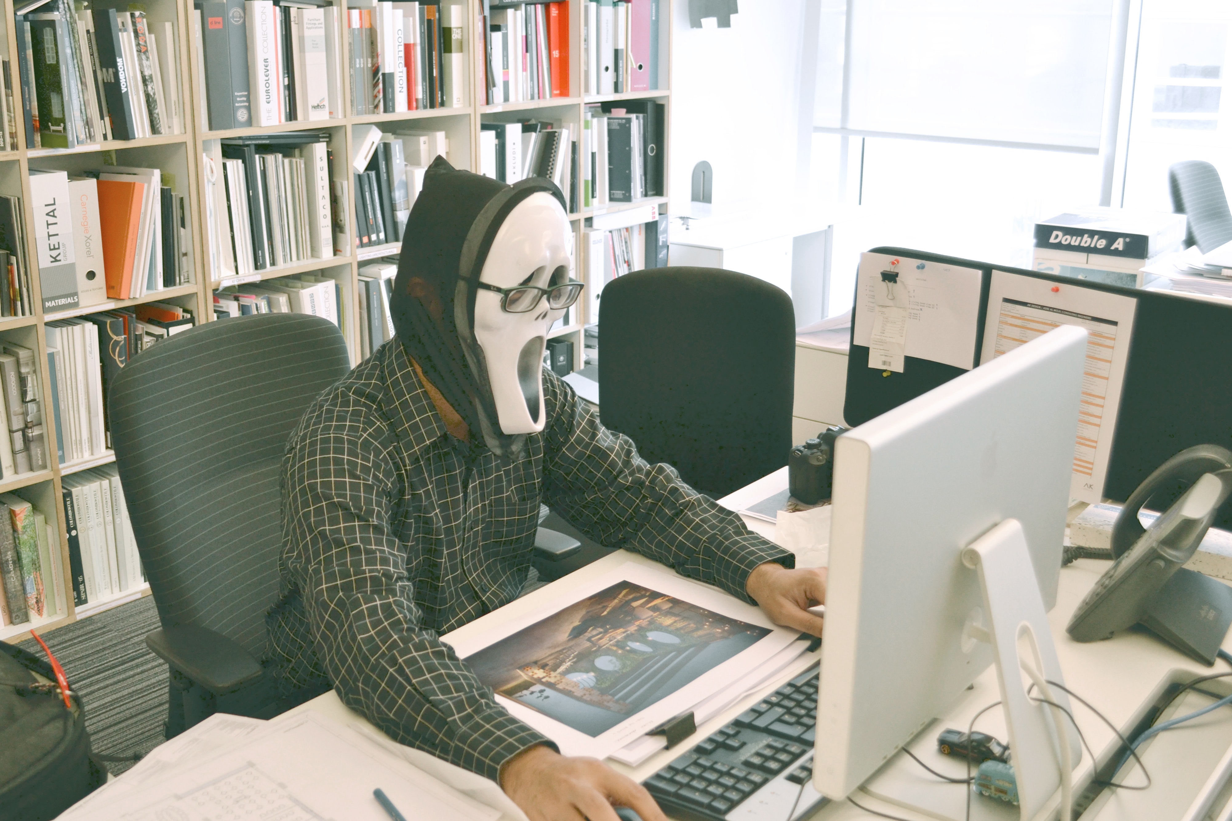 Person wearing scream mask and black dress shirt while facing computer table during daytime photo