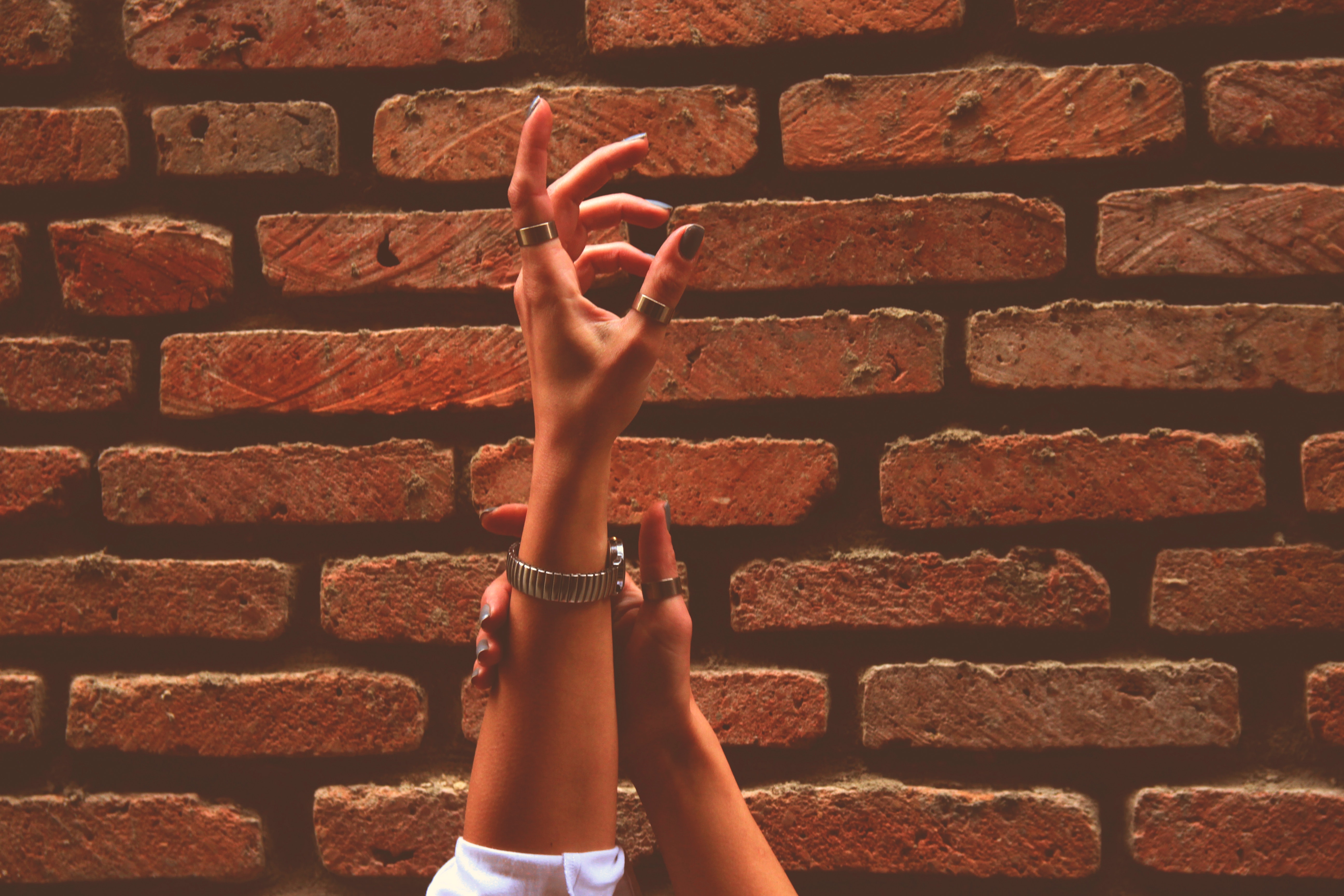 Person wearing watch and rings raising left hand near brick wall photo