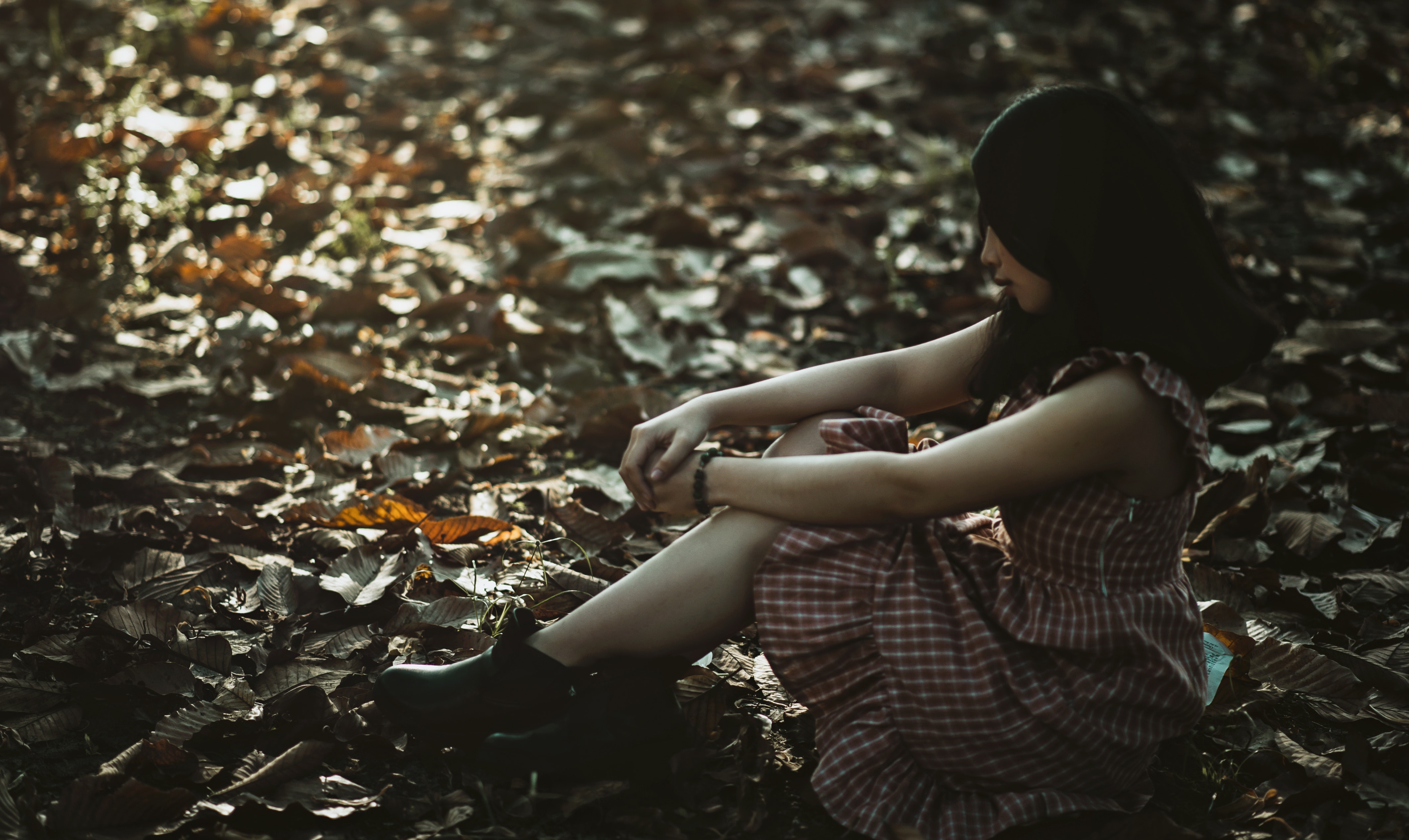 Photo of a woman sitting on the ground covered with dried leaves