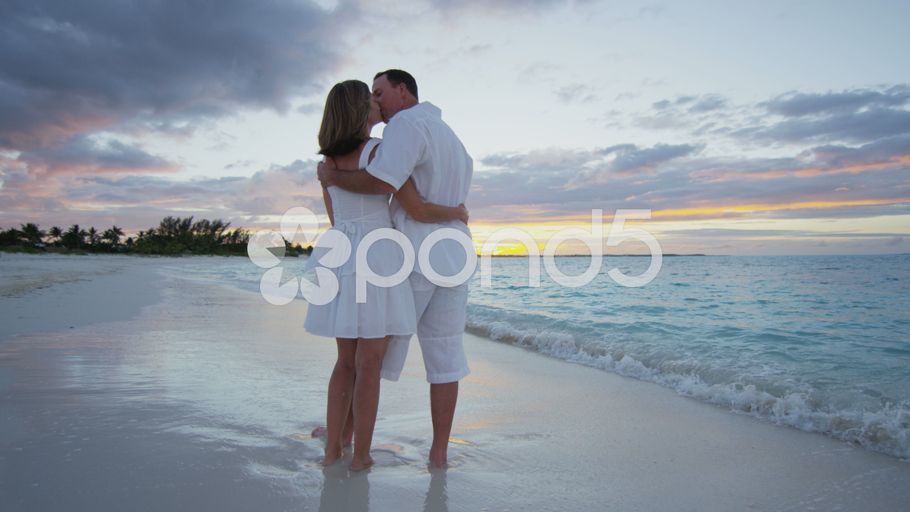 Caucasian couple wearing white clothes on a beach together at sunset ...