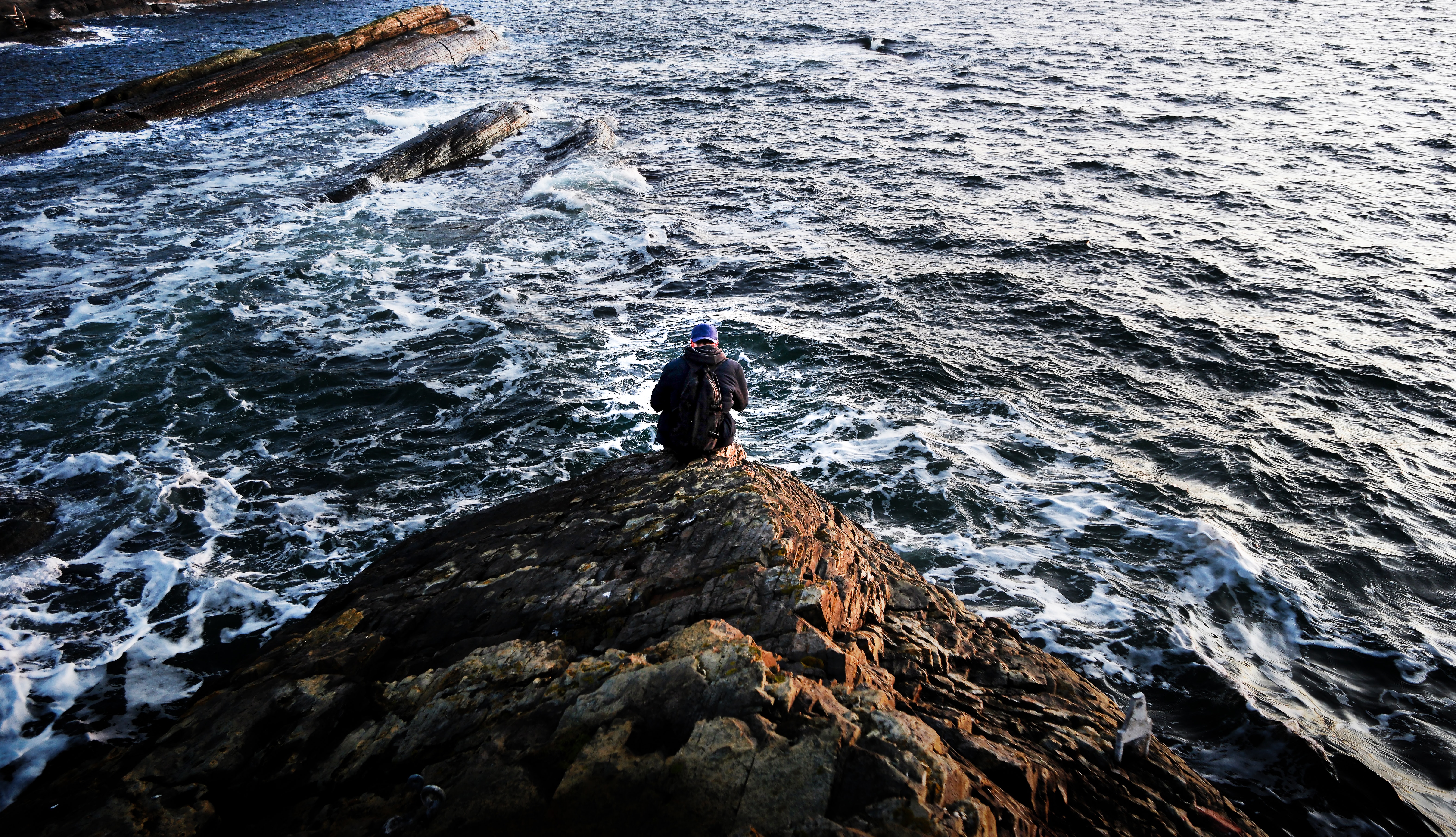 Photography of person sitting on rock near ocean