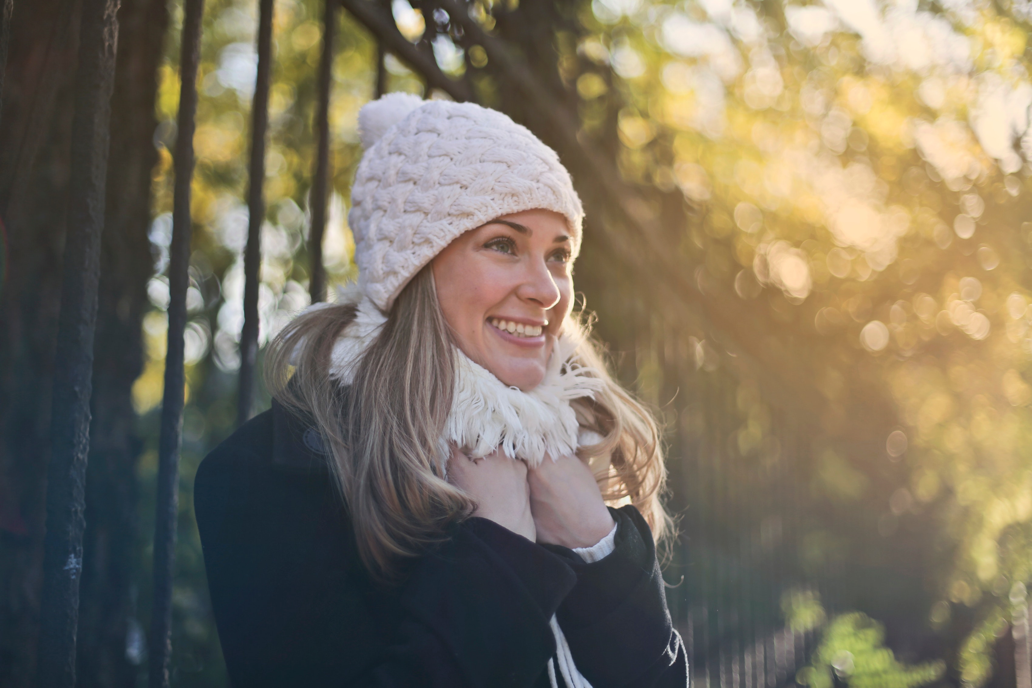 Photography of woman in black jacket and white knit cap smiling next to black metal fence
