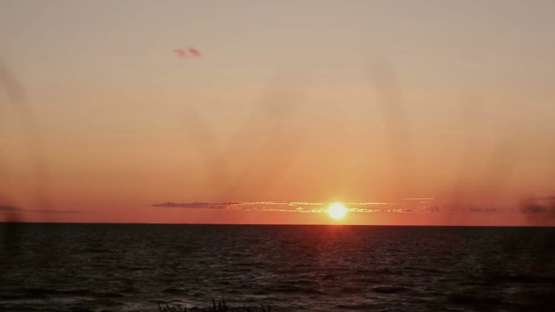 A time lapse video of pinky-orange sunset at sea side with dry grass ...